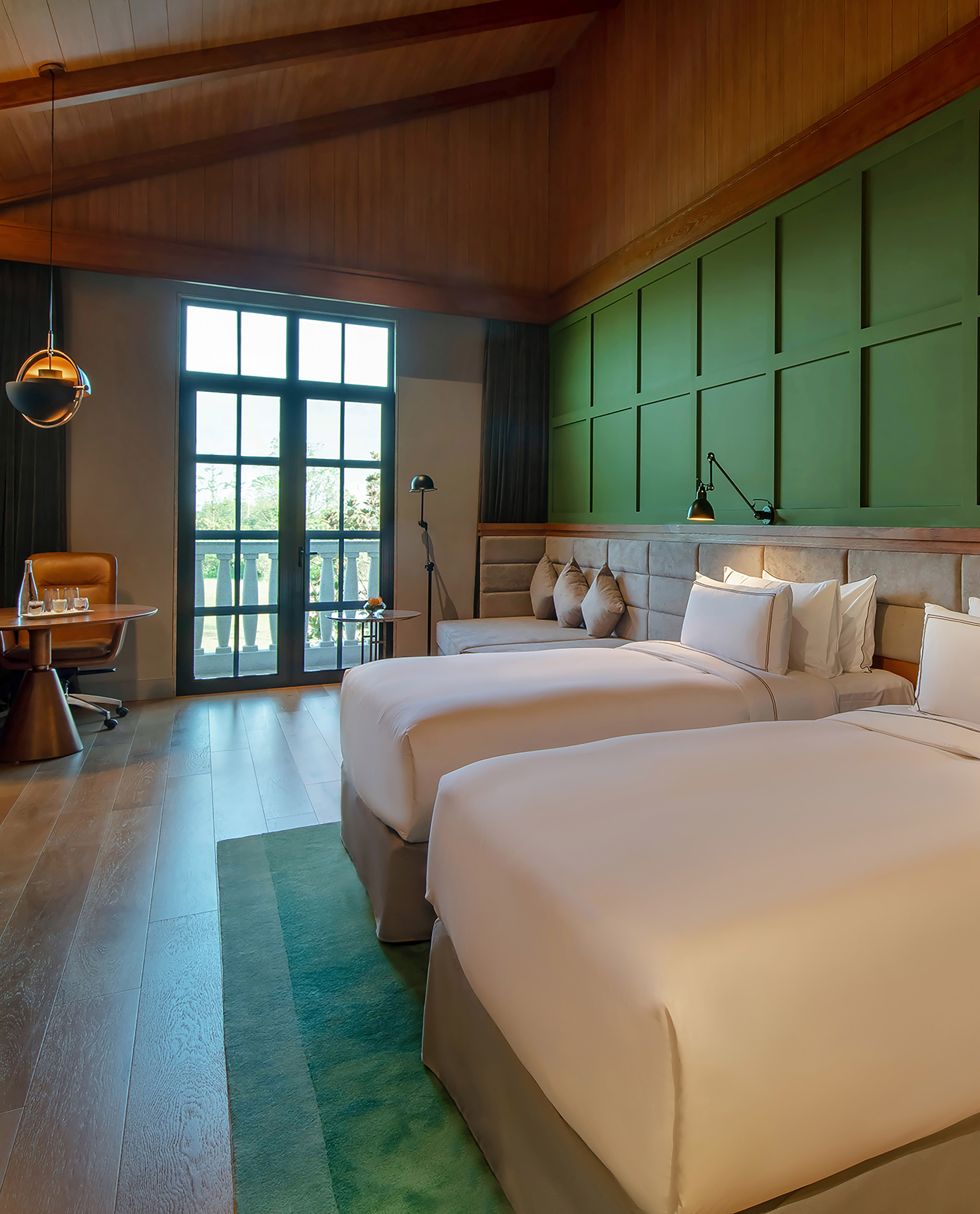 Stylish hotel room with twin beds, wood ceiling, green panel wall, and balcony.