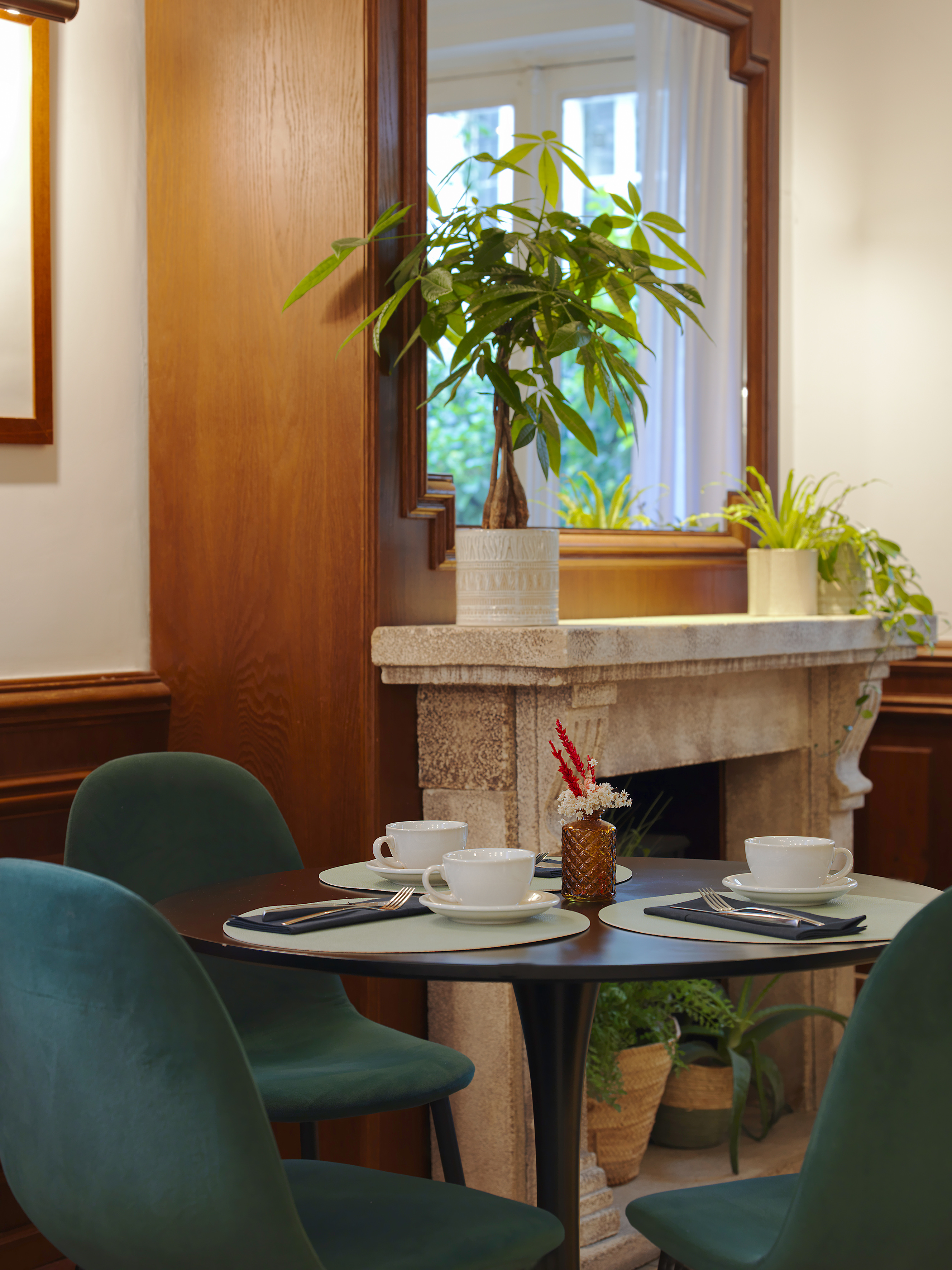 Cozy cafe dining with green chairs, table settings, fireplace, and plants.