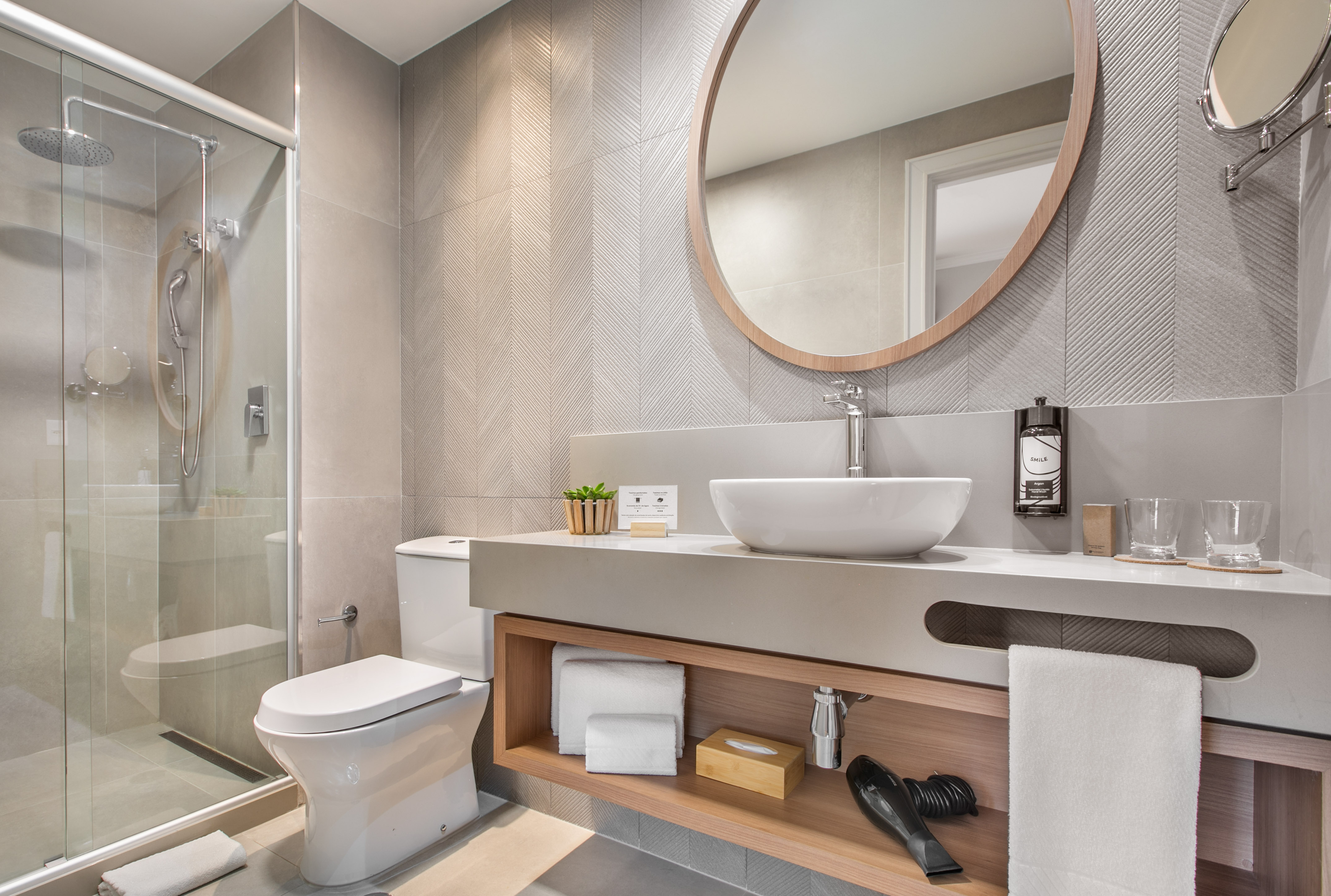Modern hotel bathroom with glass shower, floating vanity, and round mirror.