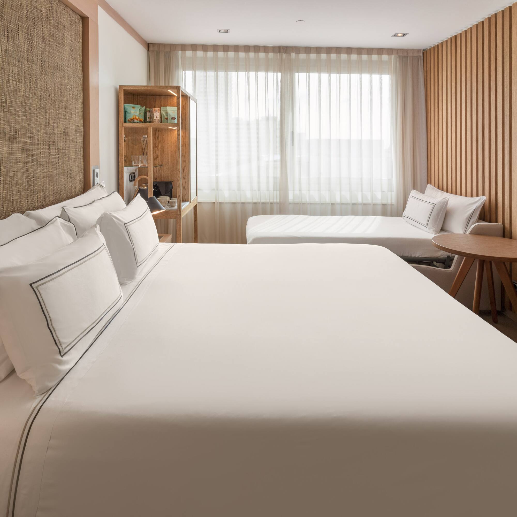 Modern hotel room with large bed, daybed, wood paneling, and bright window.