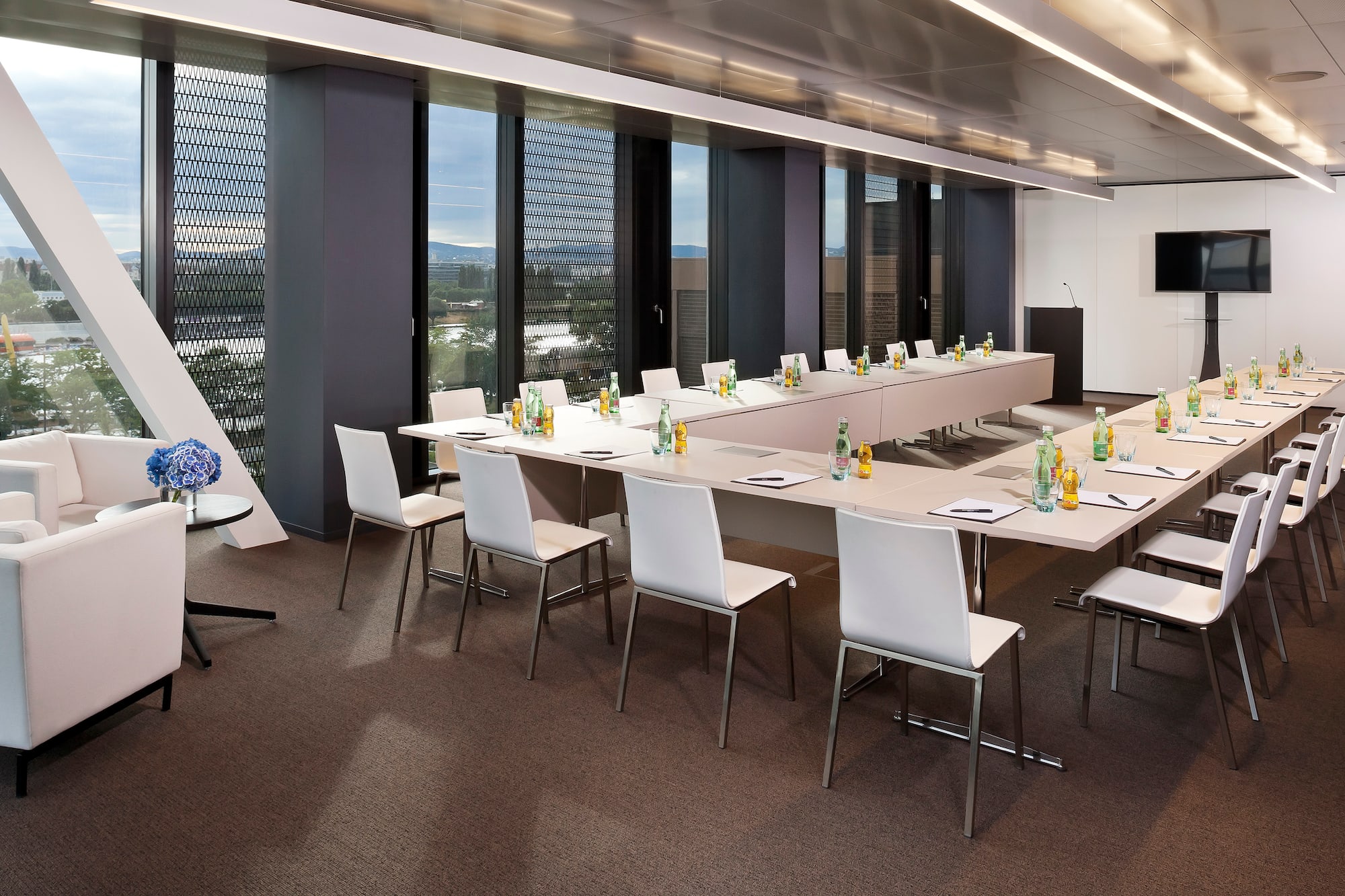 Modern conference room with U-shaped table, large windows, and lounge seating.