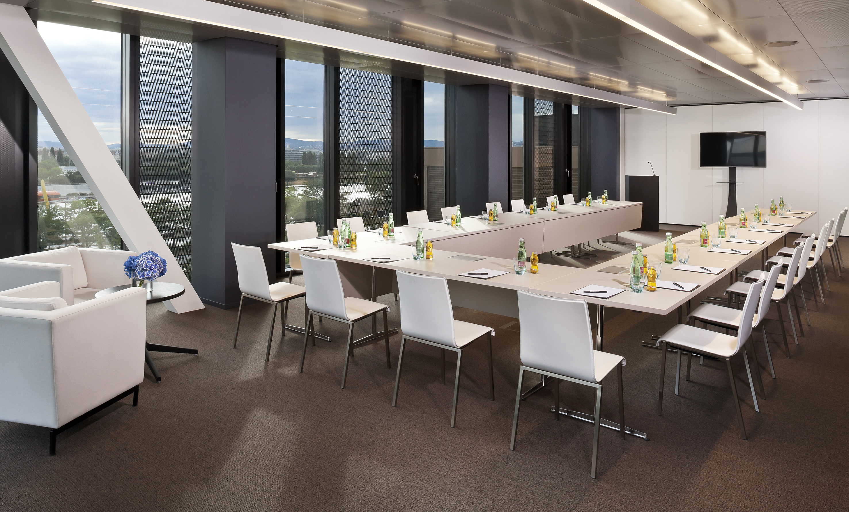 Modern conference room with U-shaped table, large windows, and lounge seating.