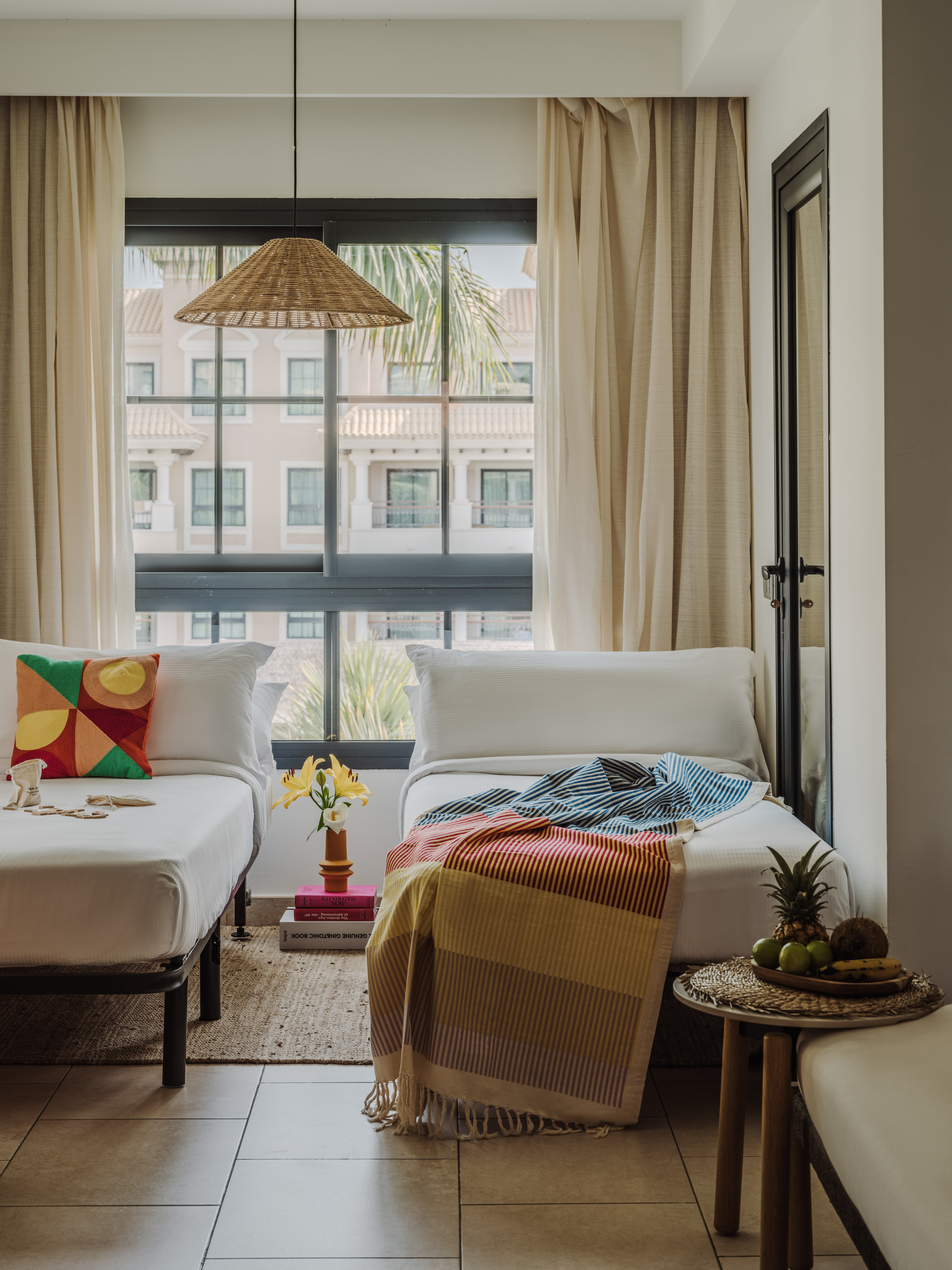 Bright twin room with tropical decor, colorful bedding, fruit, and window view.