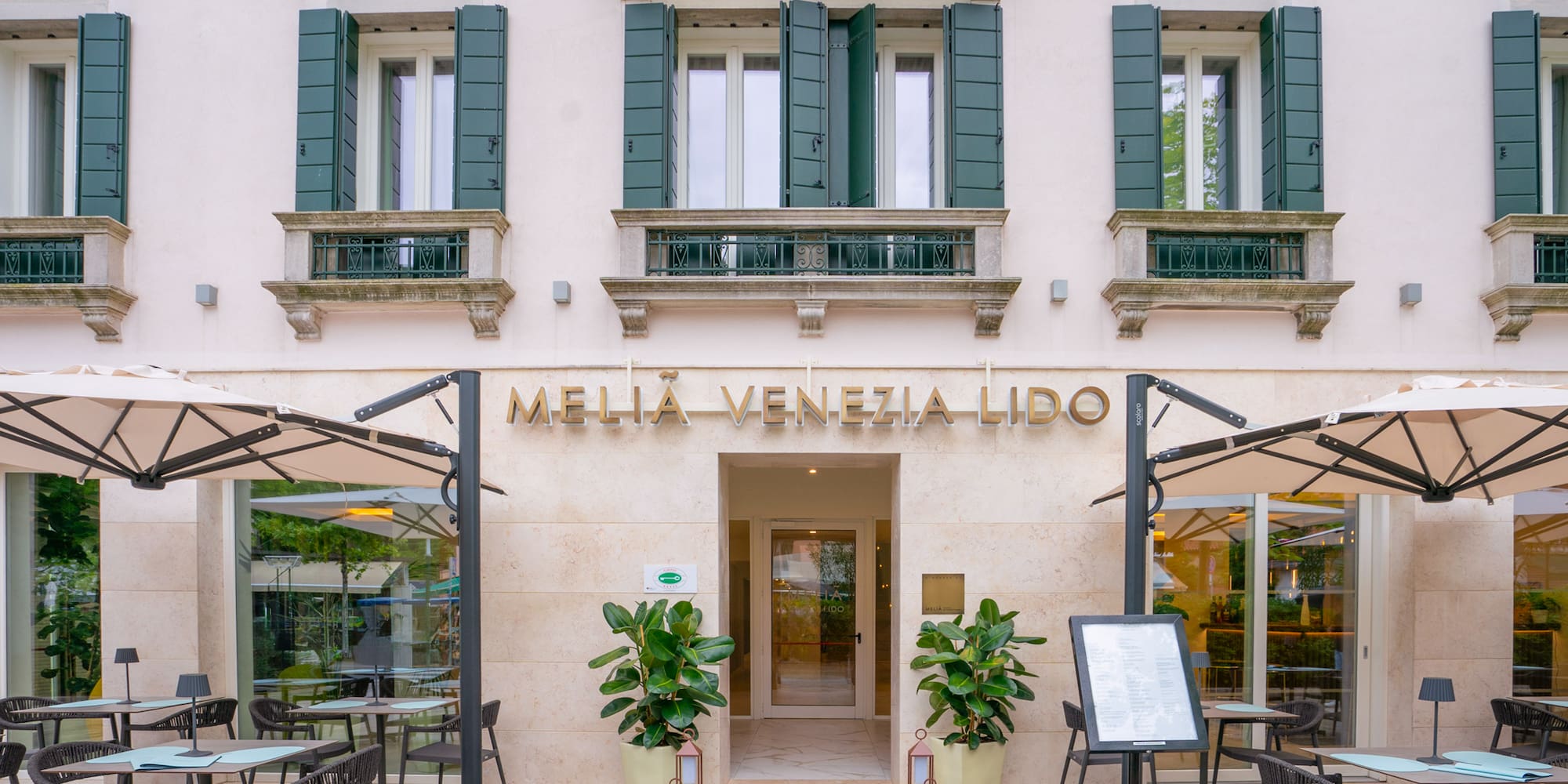 Melia Venezia Lido hotel facade, outdoor restaurant seating, green shutters.
