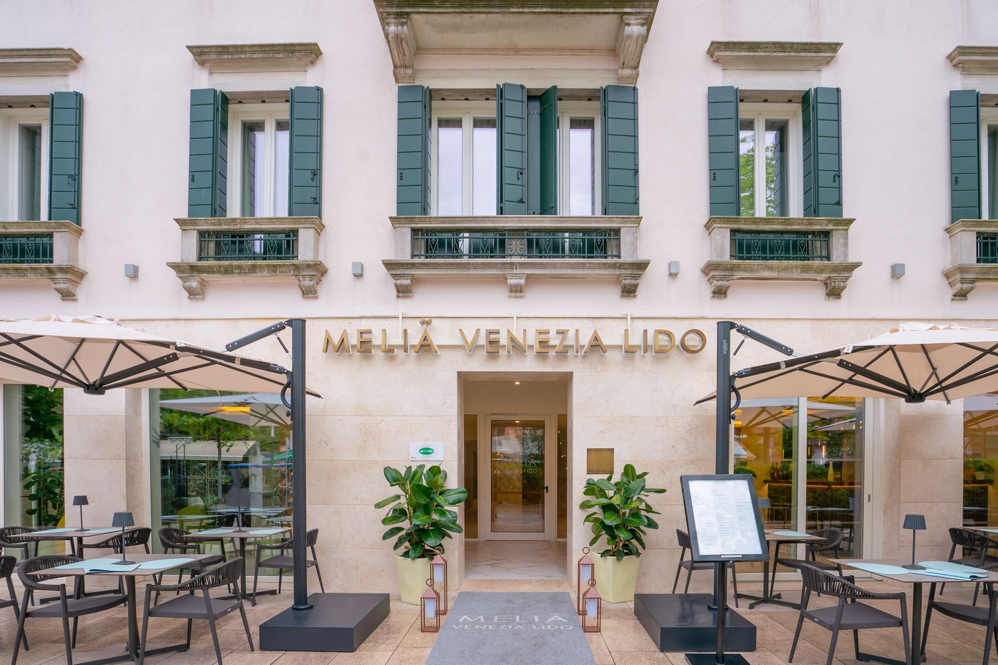 Melia Venezia Lido hotel facade, outdoor restaurant seating, green shutters.