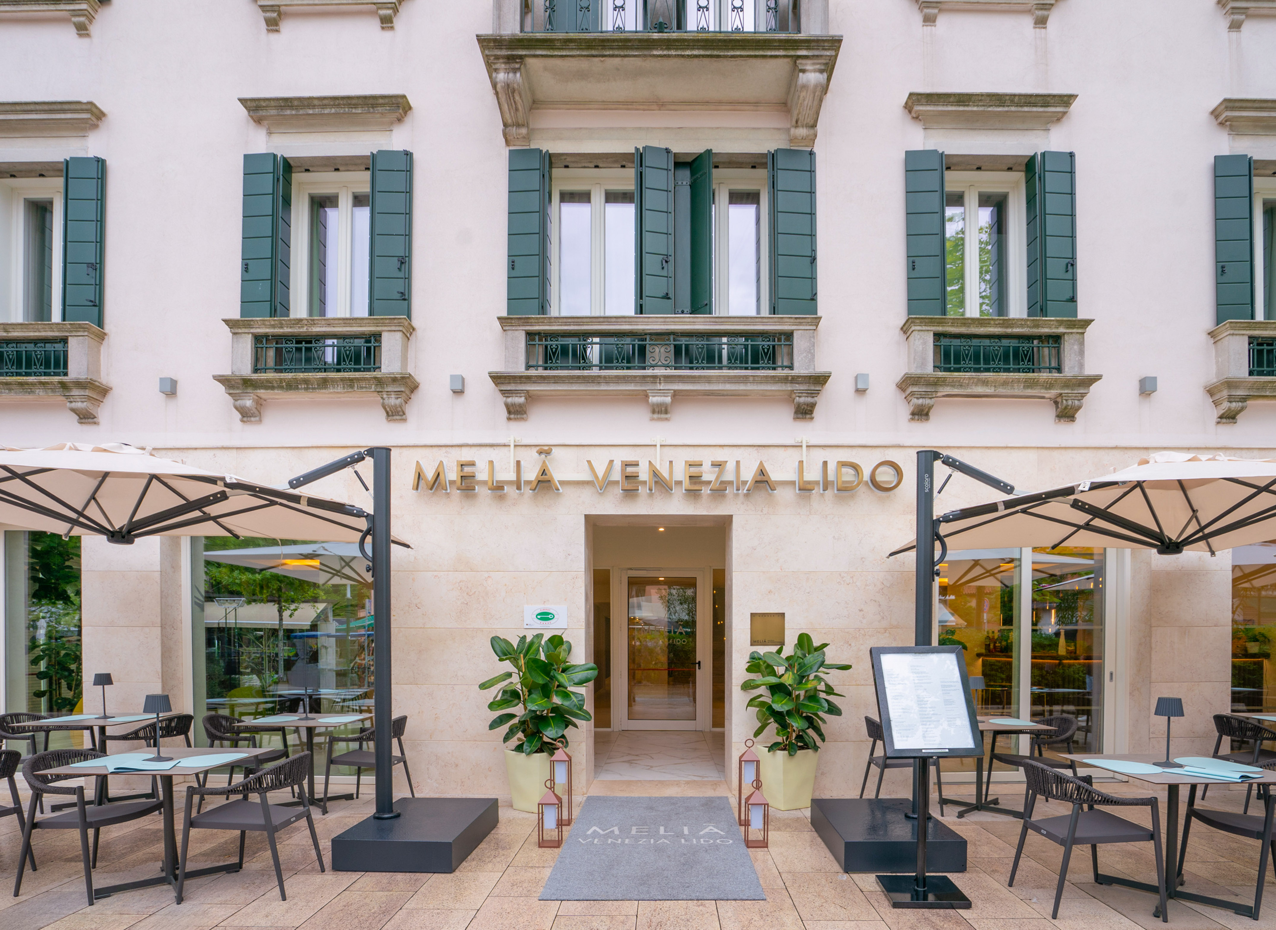 Melia Venezia Lido hotel facade, outdoor restaurant seating, green shutters.