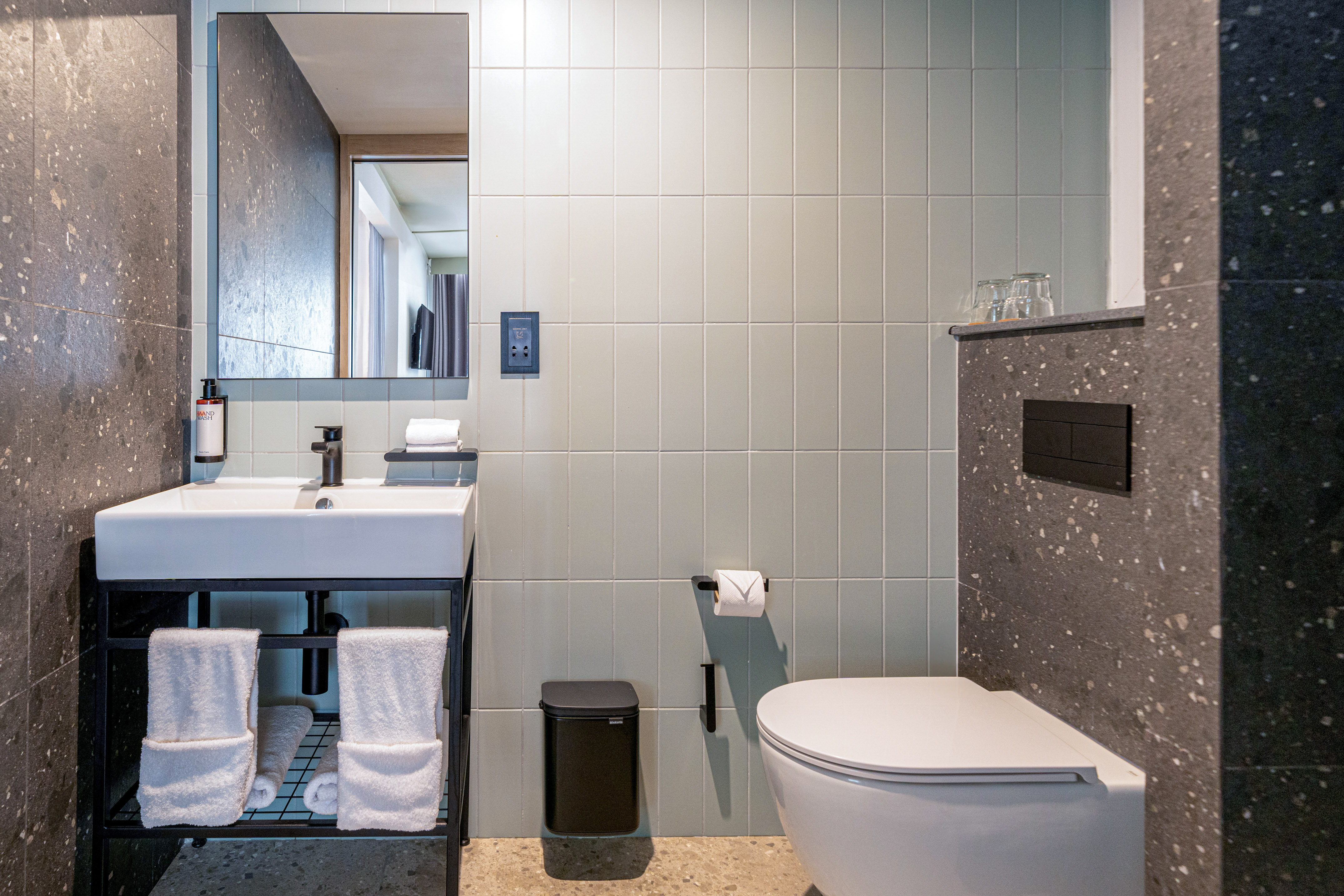 Modern bathroom with white sink, mirror, toilet, and grey-green tiled walls.