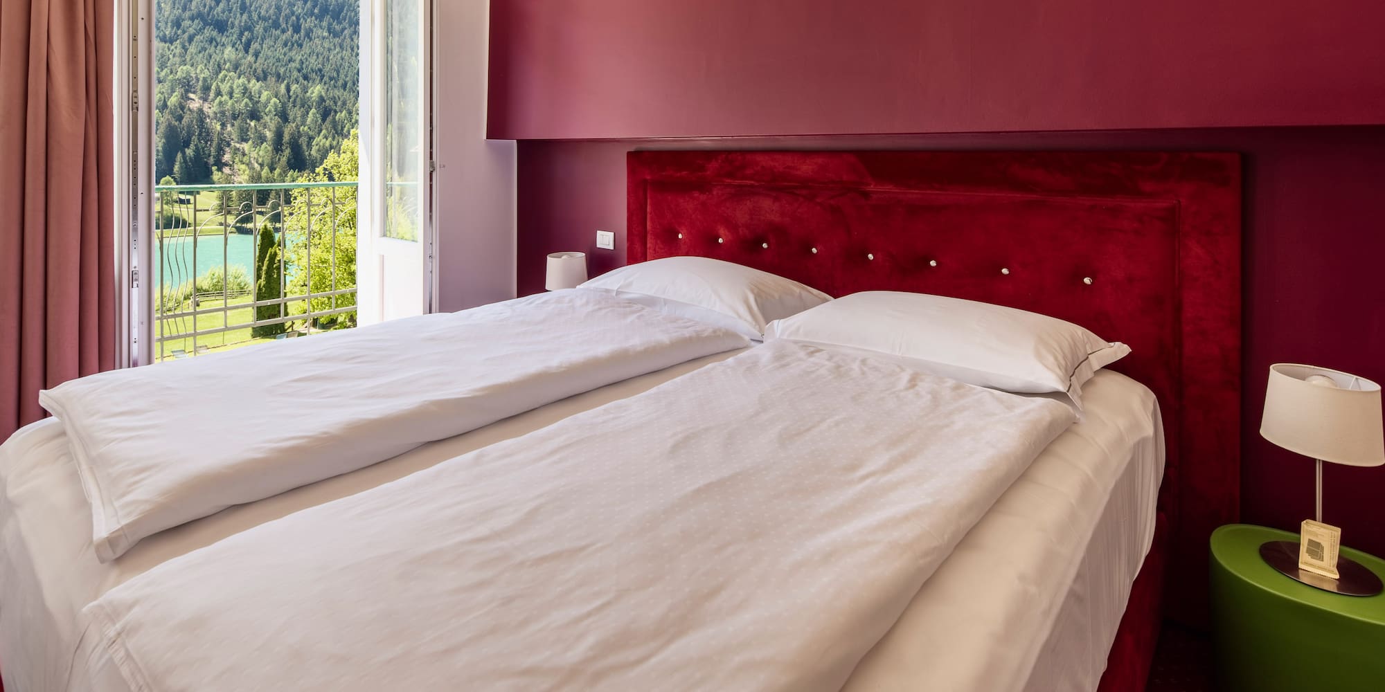 Red hotel bedroom with twin beds, balcony and scenic mountain lake view.