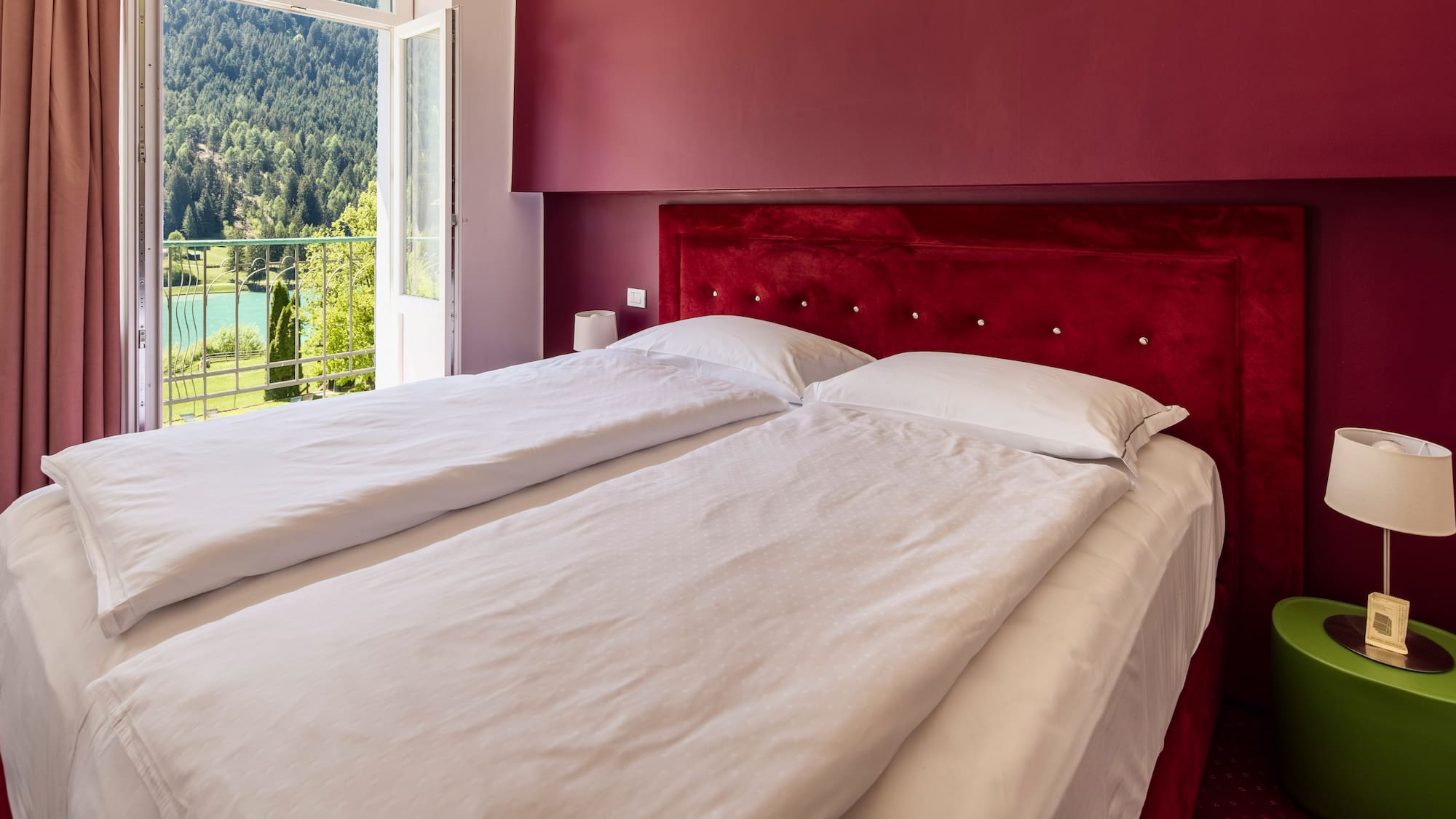 Red hotel bedroom with twin beds, balcony and scenic mountain lake view.