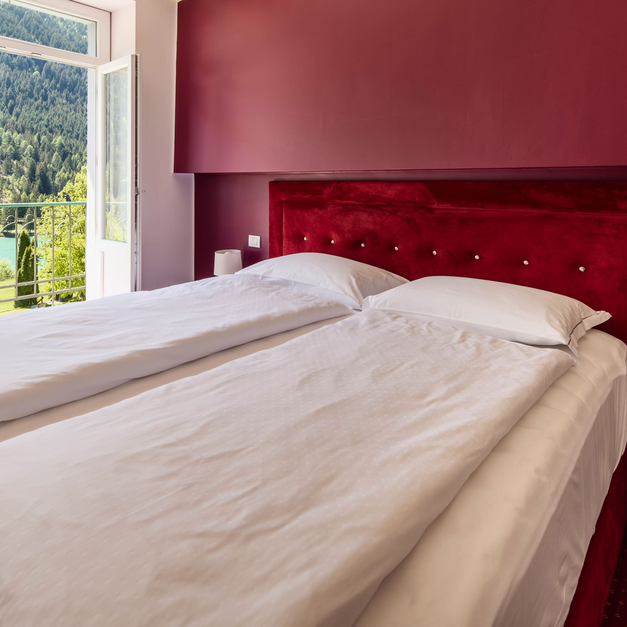 Red hotel bedroom with twin beds, balcony and scenic mountain lake view.