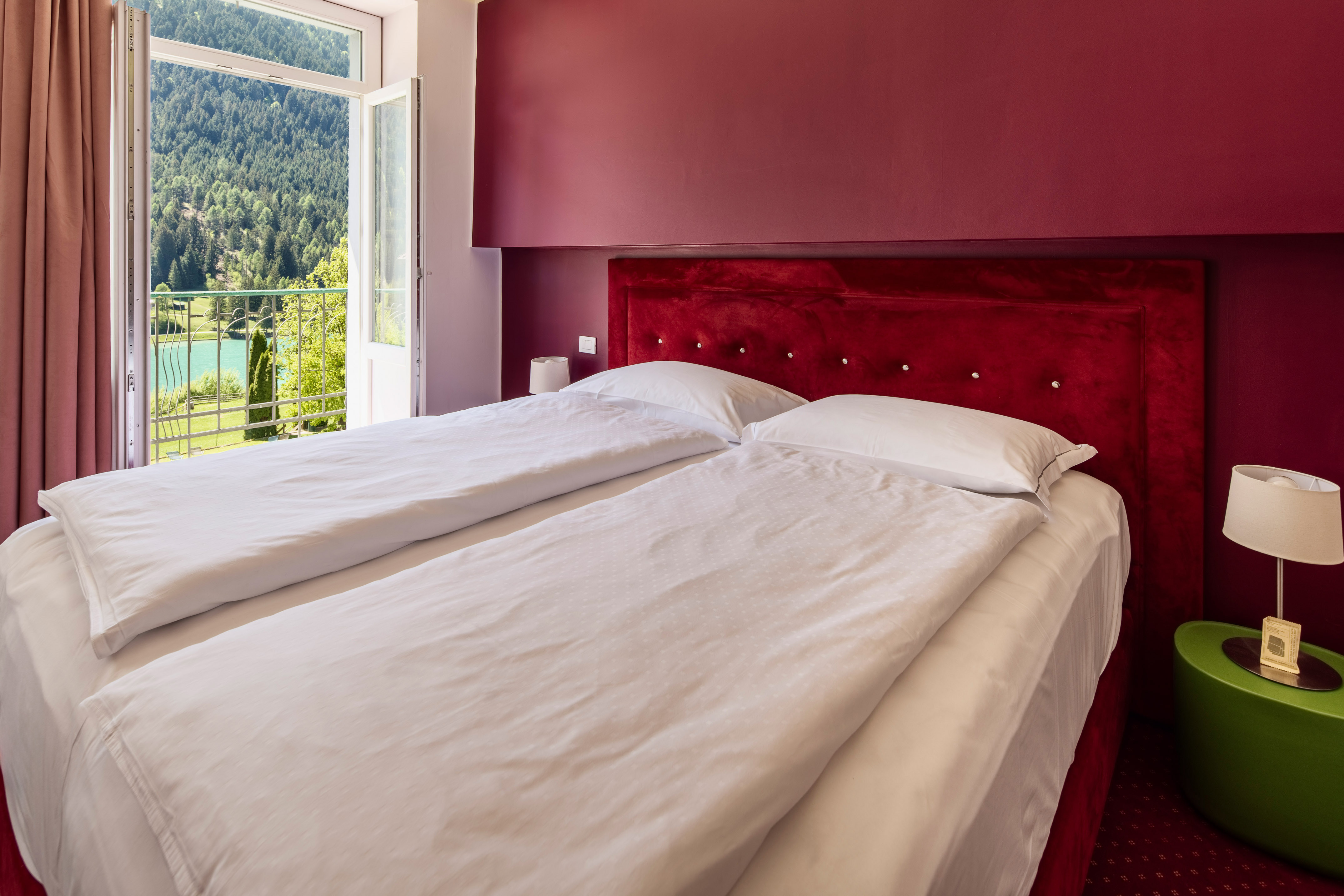 Red hotel bedroom with twin beds, balcony and scenic mountain lake view.