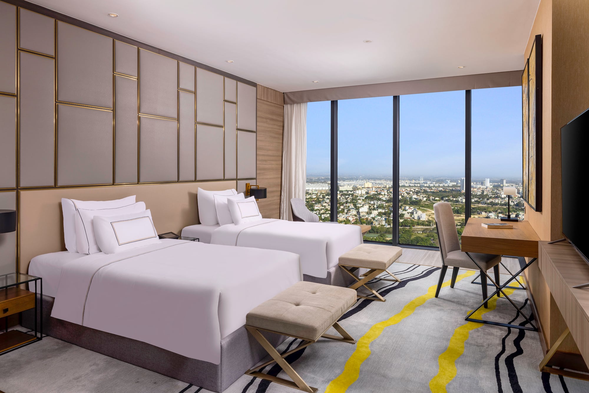 Modern hotel room with twin beds, city view, work desk, and stylish decor.
