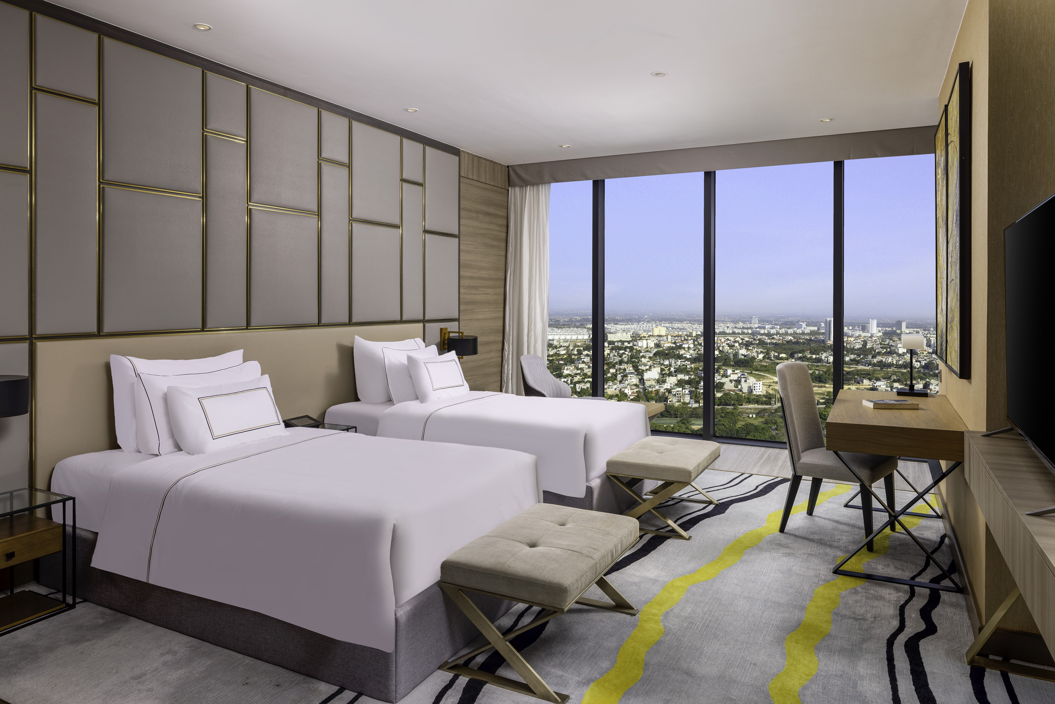 Modern hotel room with twin beds, city view, work desk, and stylish decor.