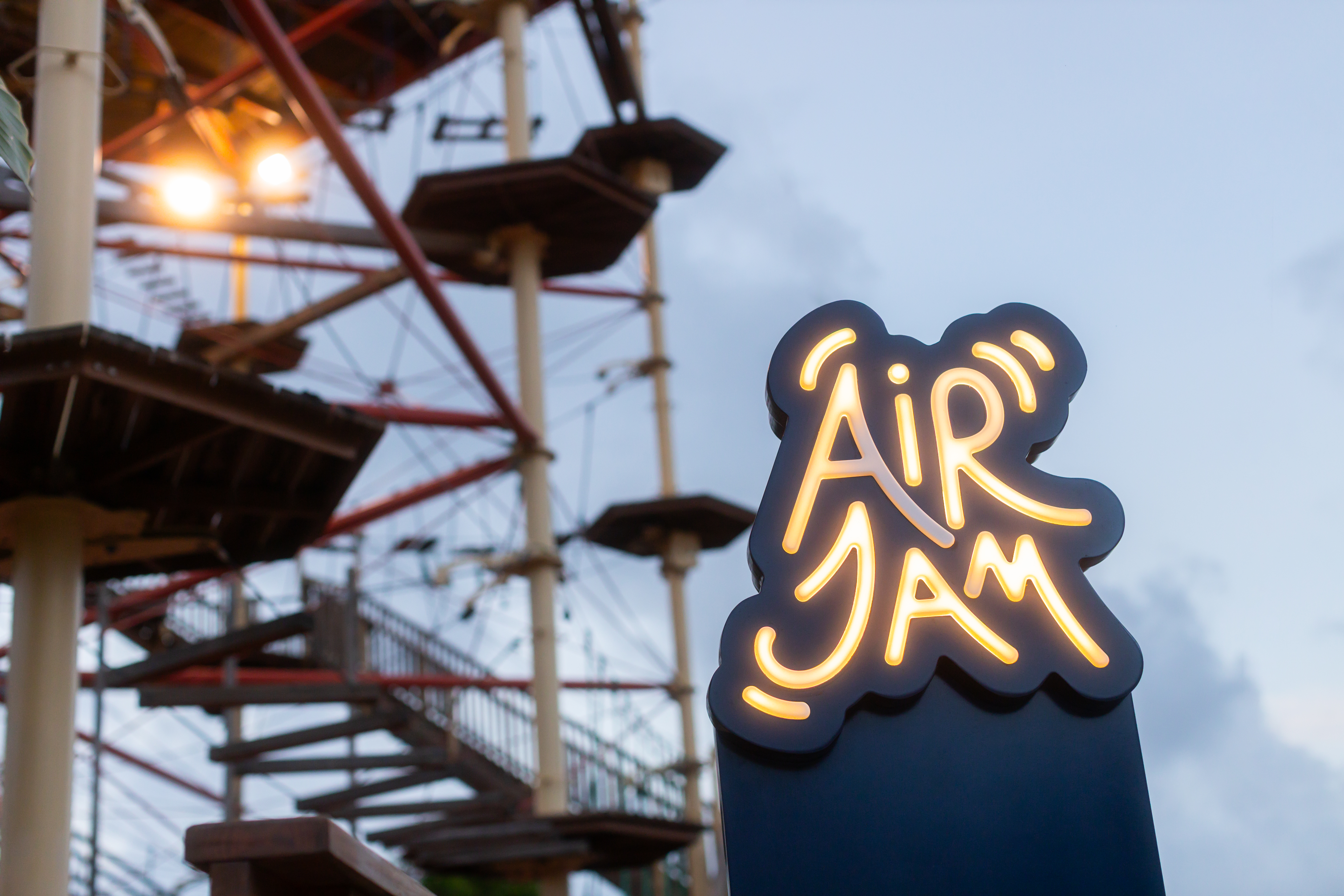 Illuminated Air Jam sign against an outdoor ropes course structure.