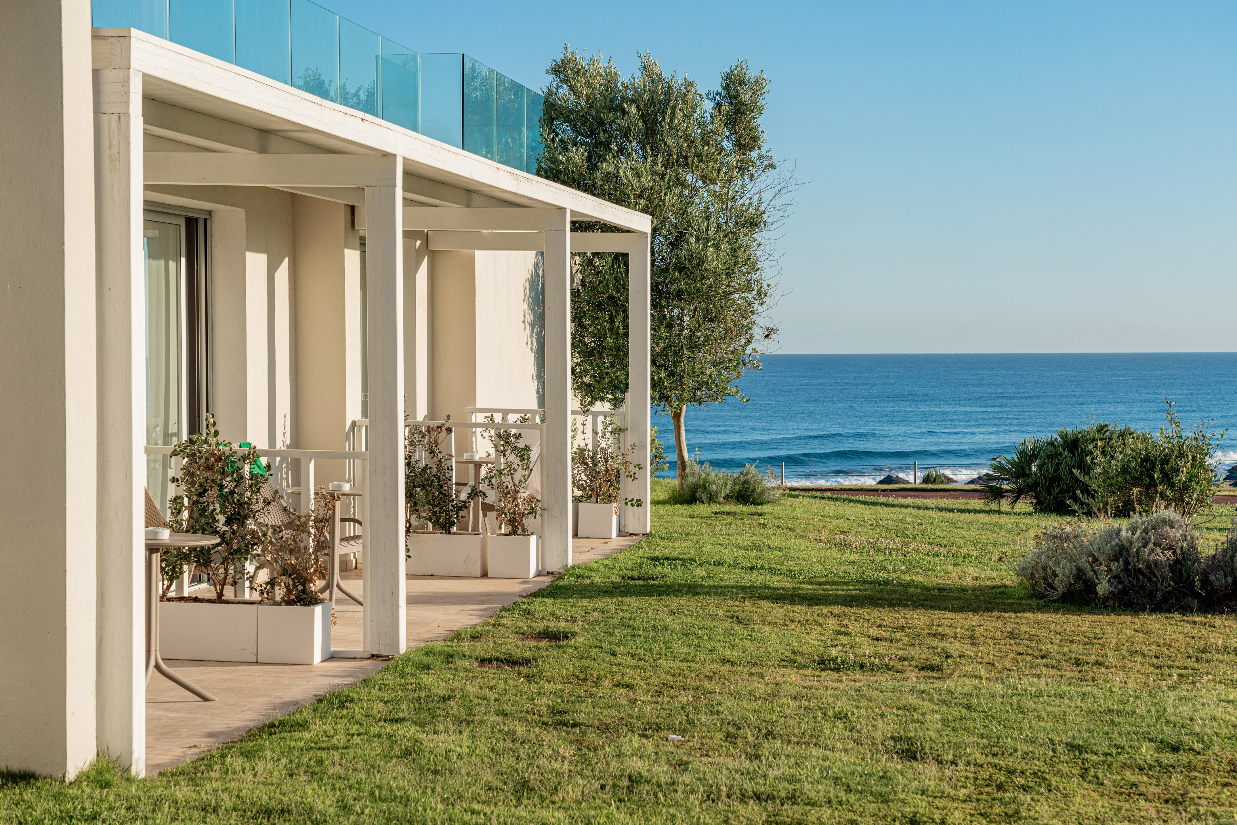 Beachfront hotel terraces with white pergolas, green lawn, and ocean.