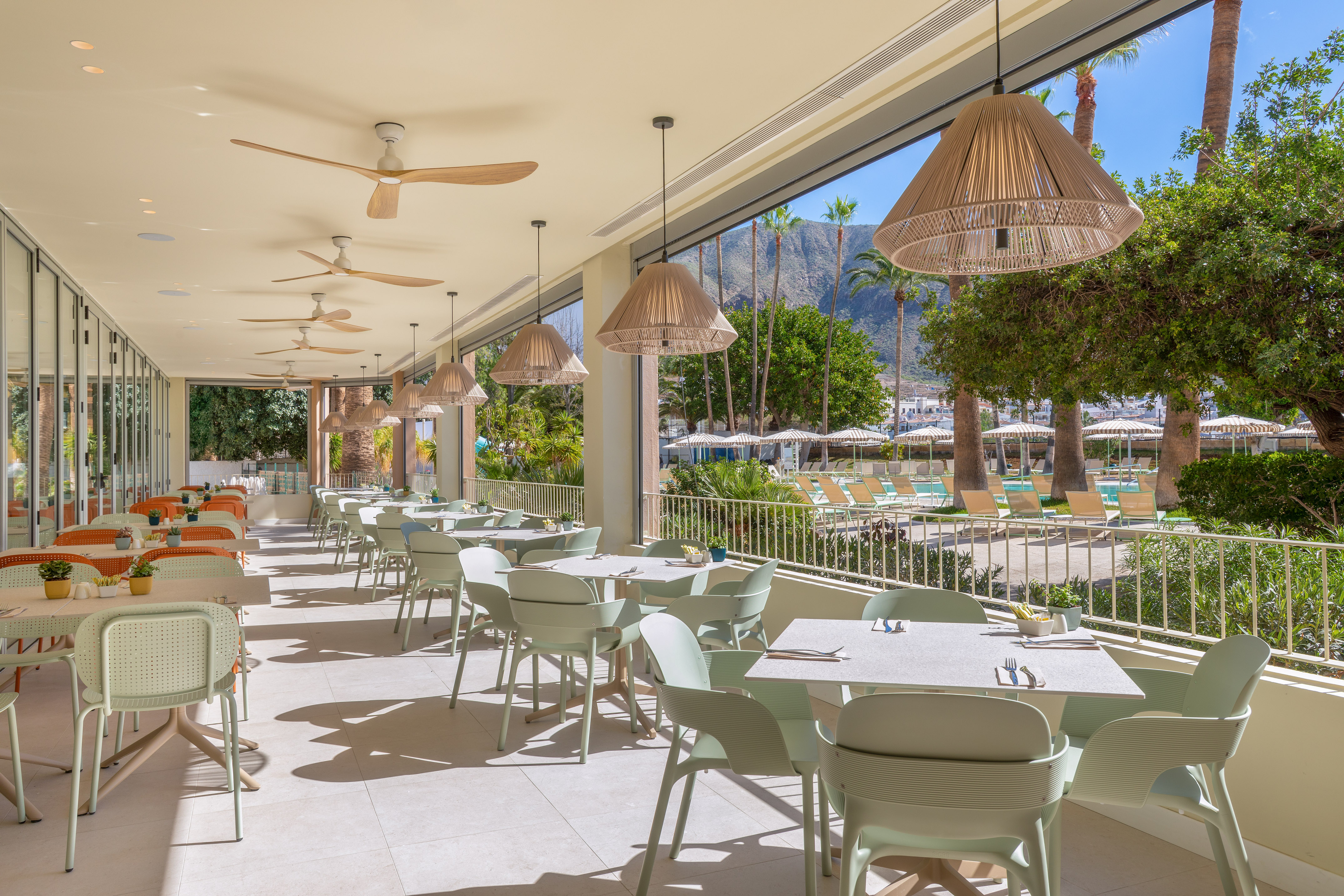 Outdoor resort dining with light green chairs, ceiling fans, and pool view.
