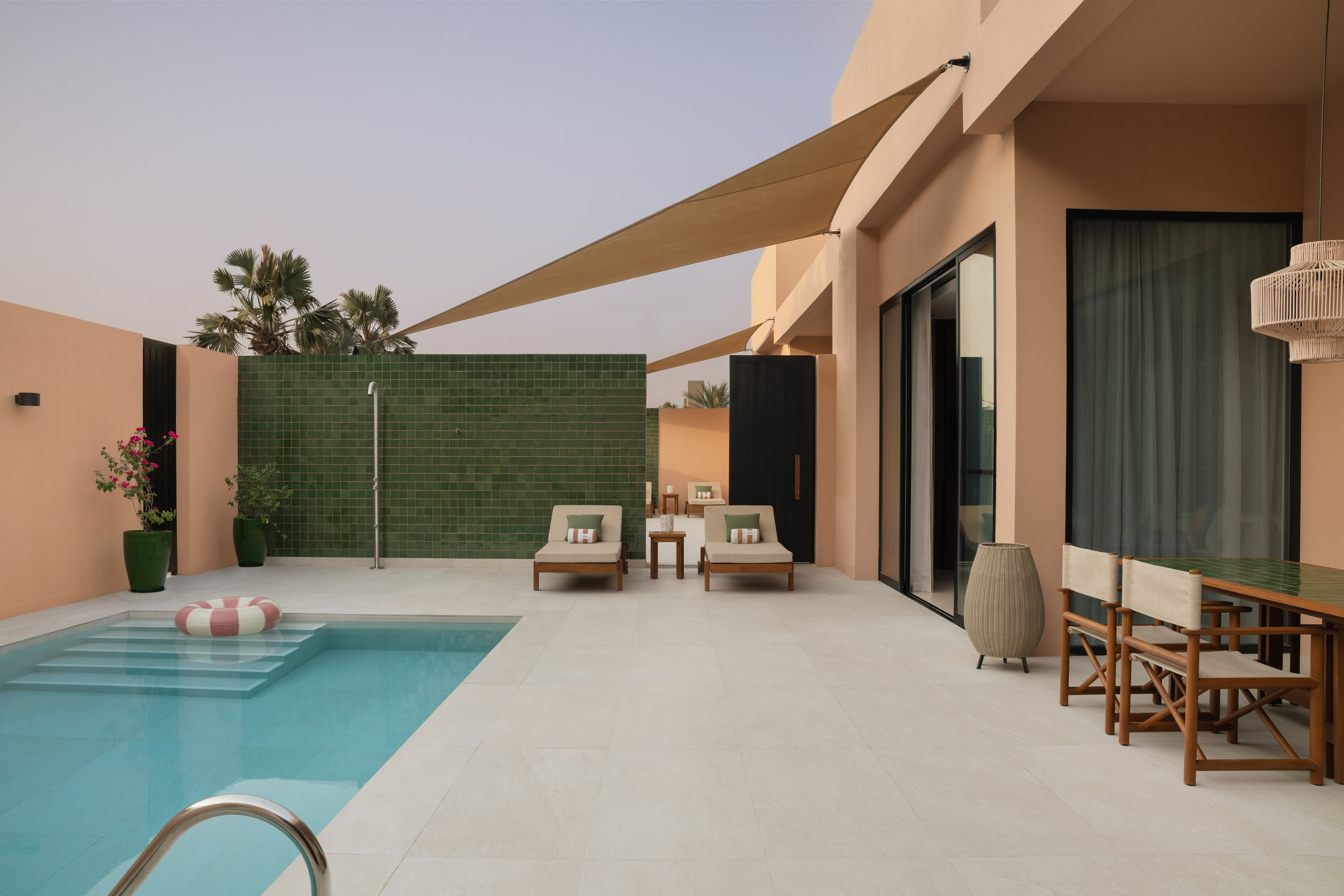 Modern private pool patio with sun shade, lounge chairs, and peach villa.