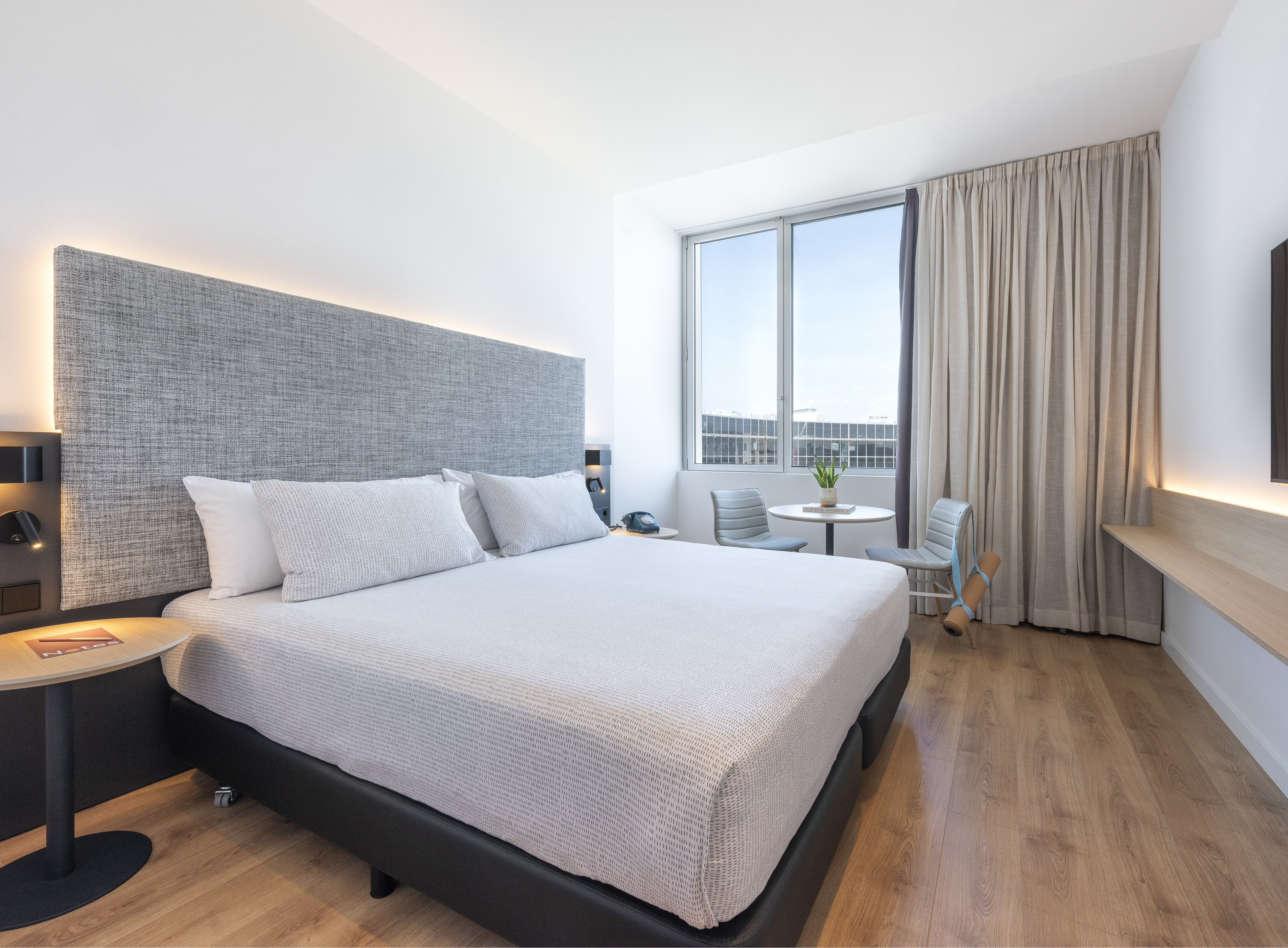 Modern hotel room with queen bed, backlit headboard, and wood floors.