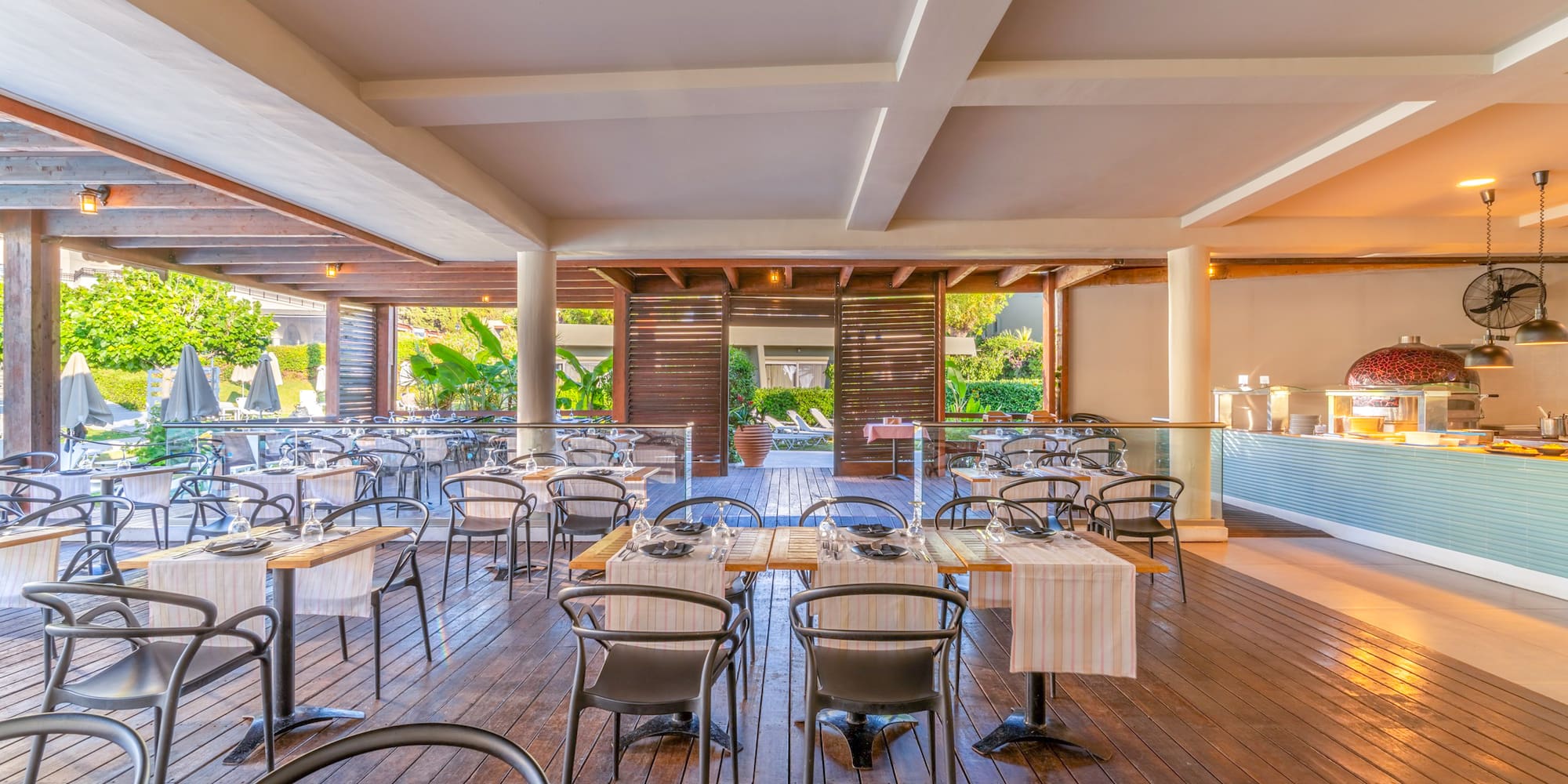 Al fresco resort restaurant with wooden deck, set tables, and a buffet.