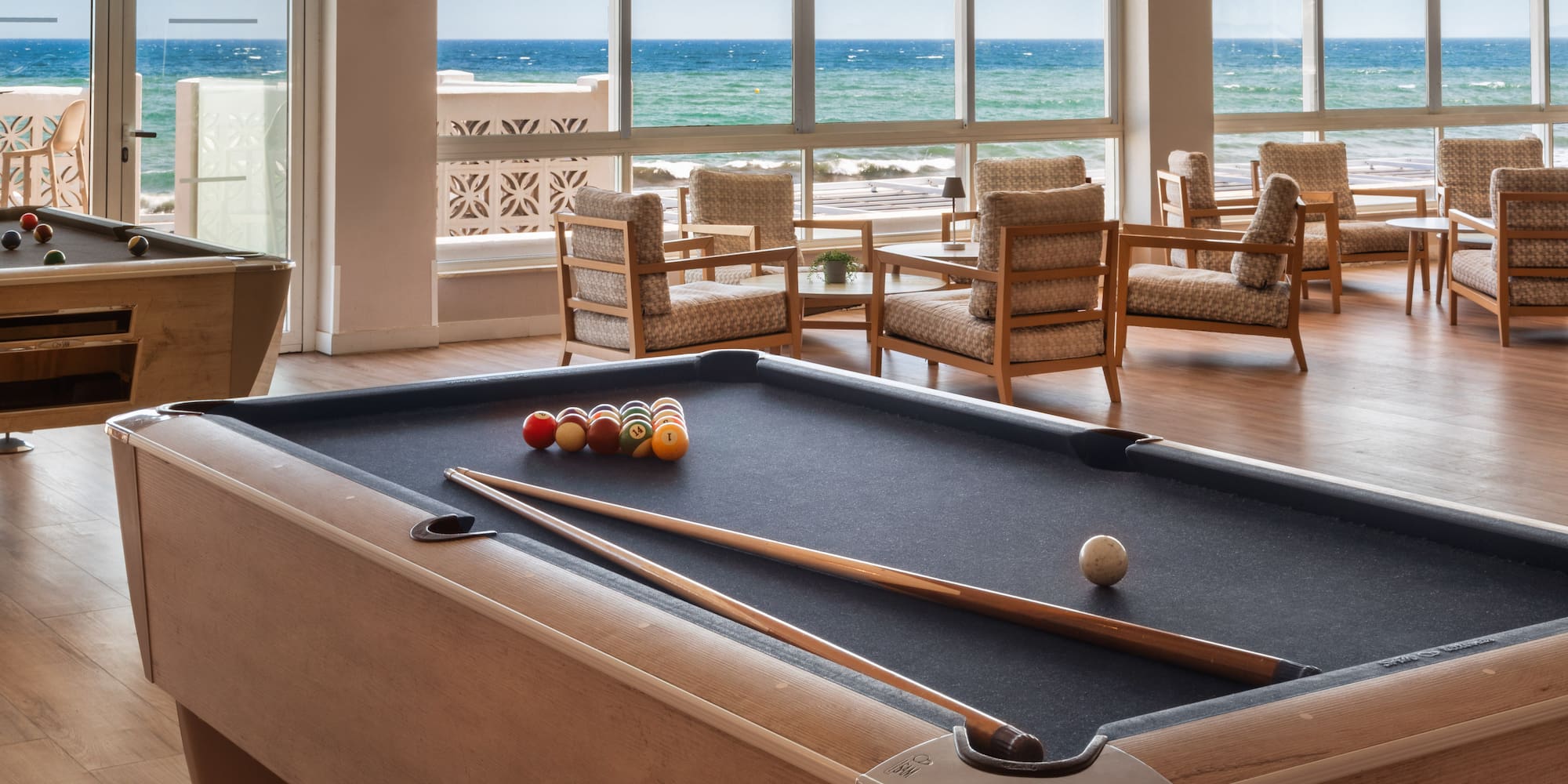 a pool table with balls and sticks in a room with chairs and a view of the ocean