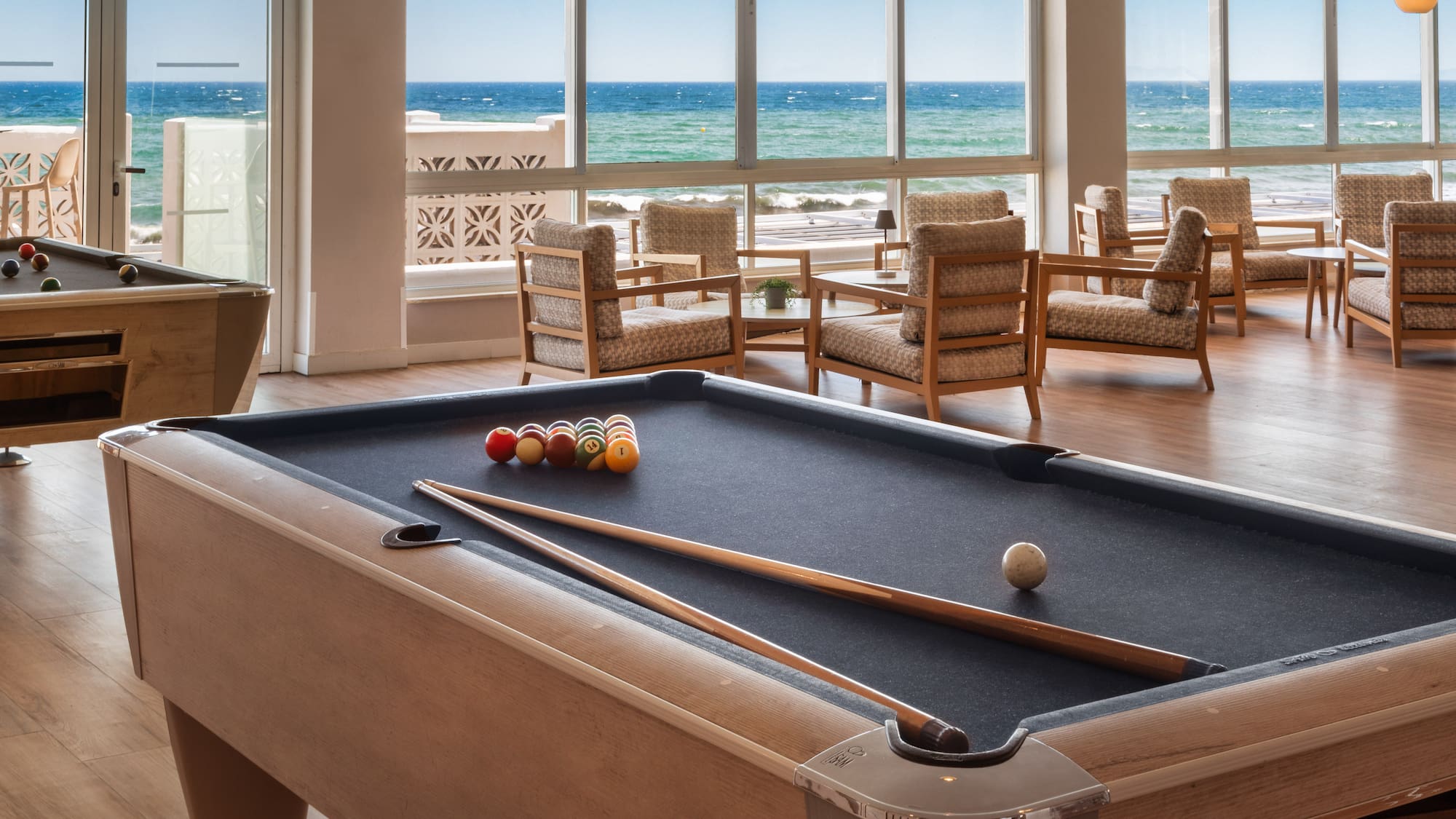 a pool table with balls and sticks in a room with chairs and a view of the ocean