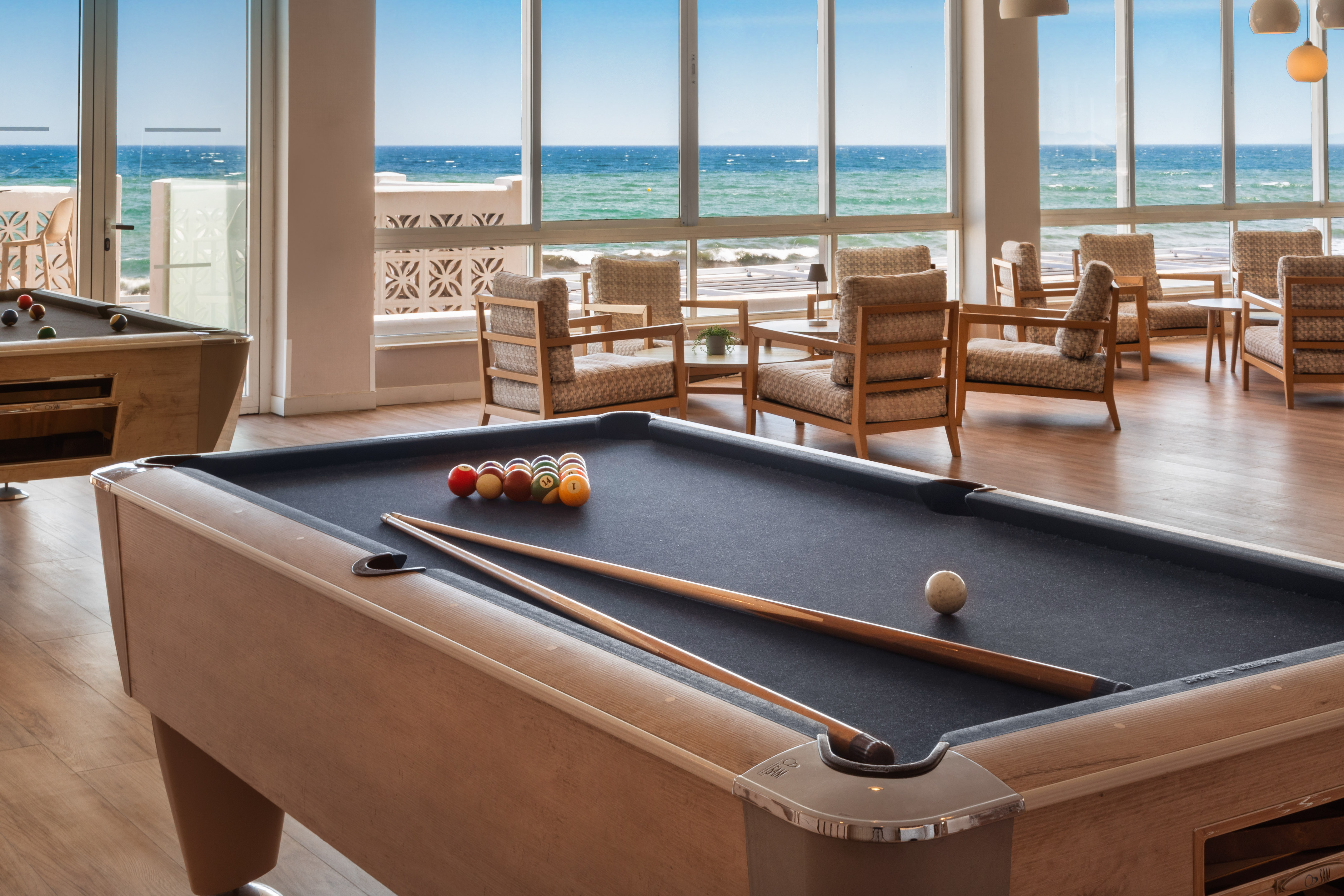 a pool table with balls and sticks in a room with chairs and a view of the ocean