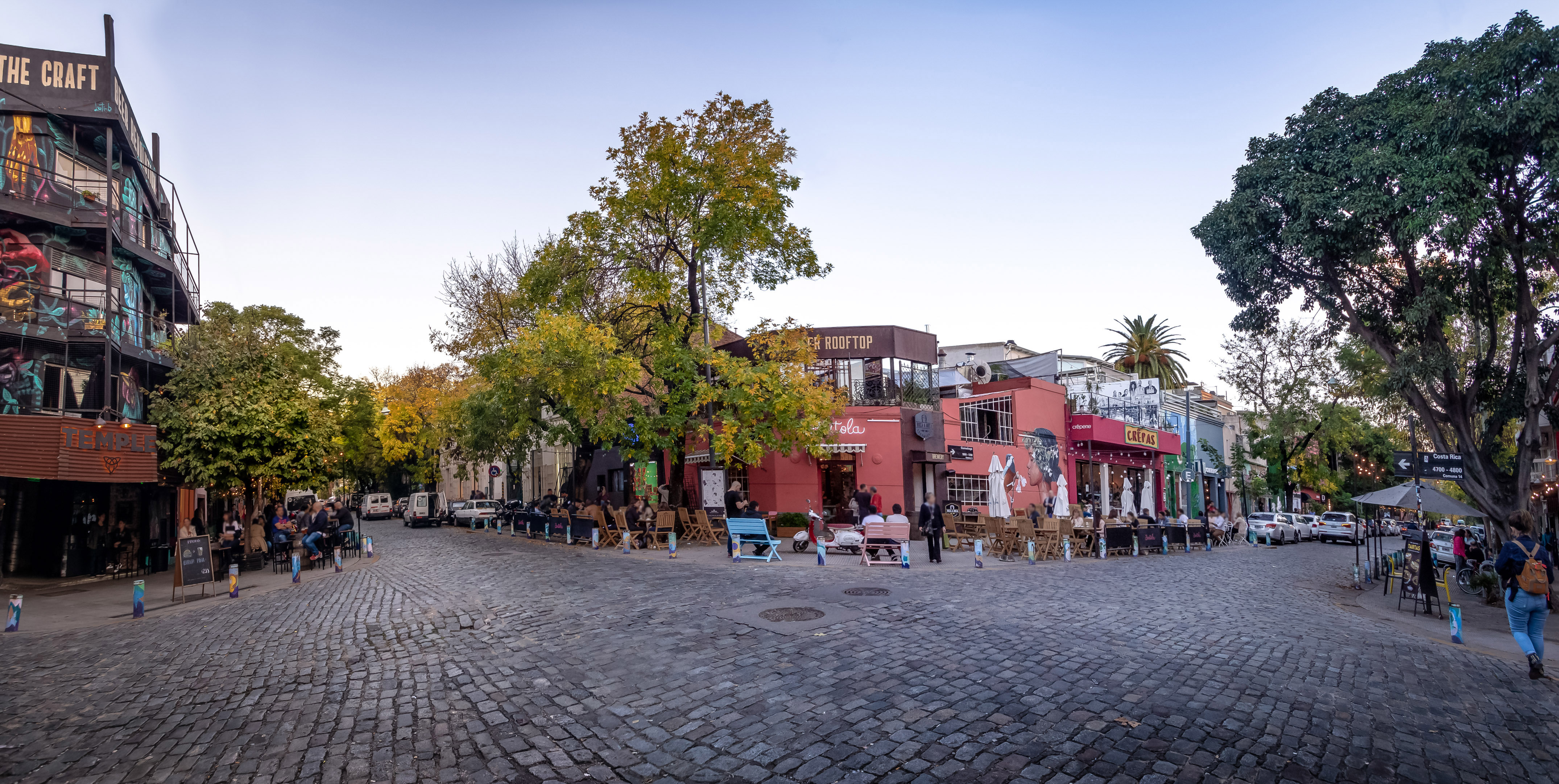 Lively cobblestone plaza with outdoor cafes, diners, and colorful buildings at dusk.