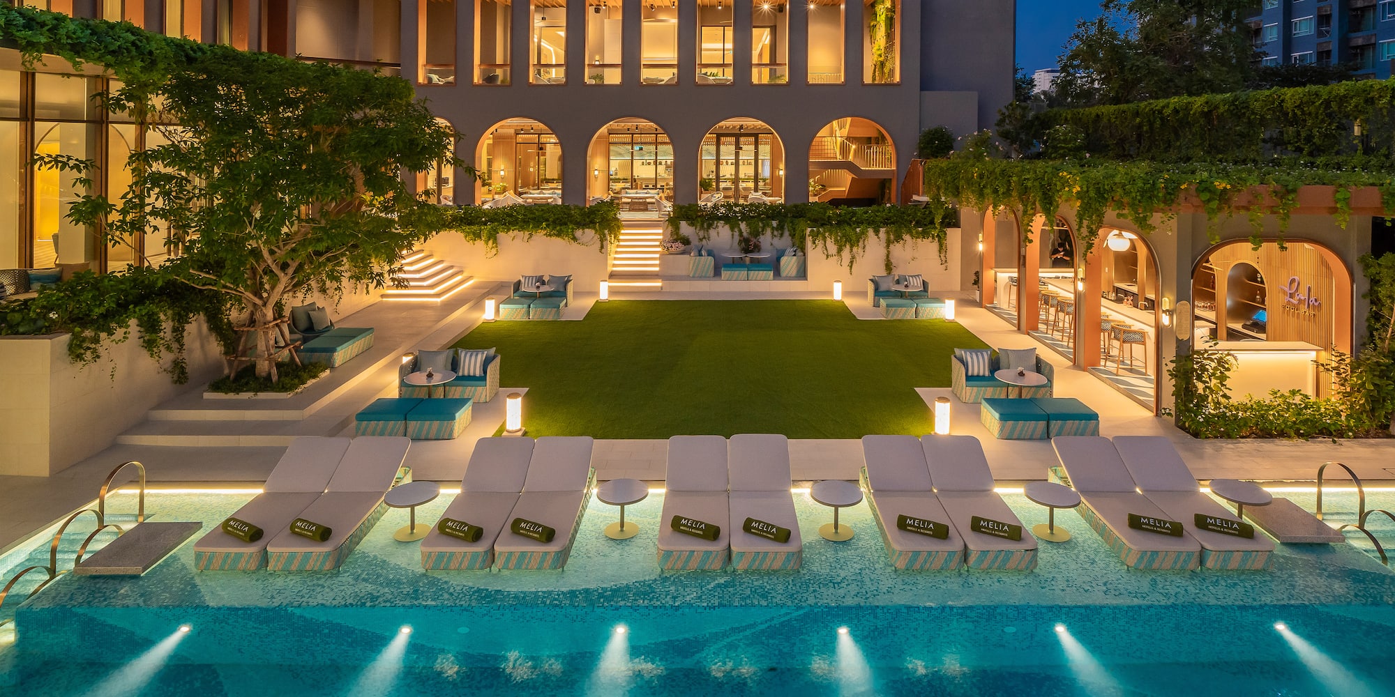 a pool with lounge chairs and trees in front of a building