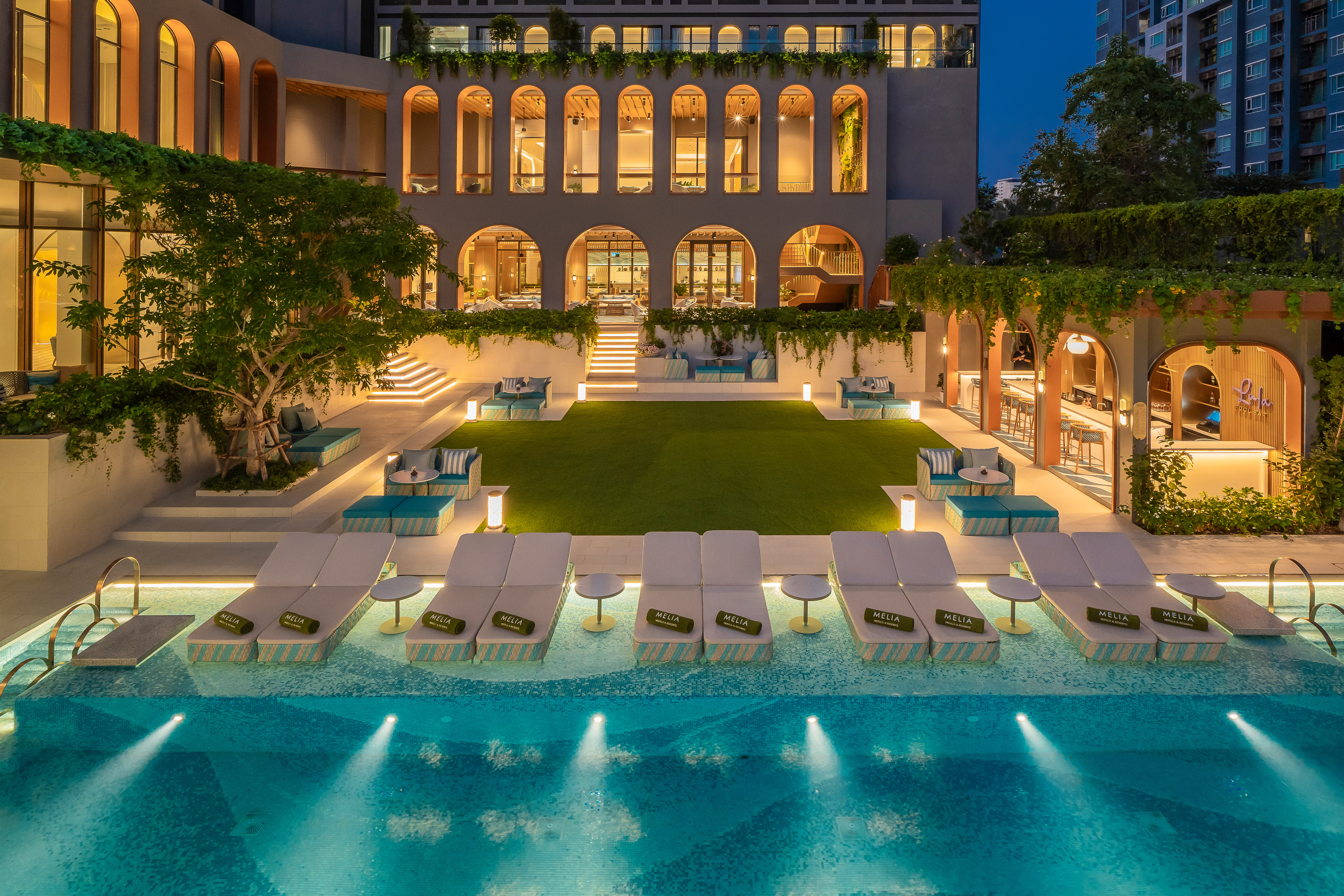 a pool with lounge chairs and trees in front of a building