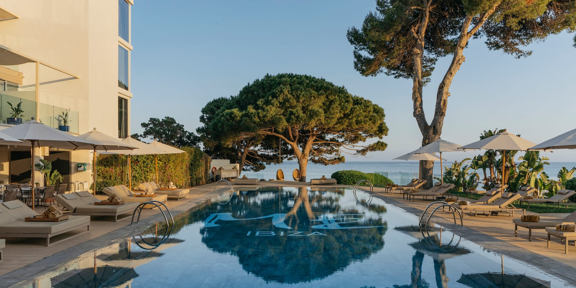 a pool with umbrellas and chairs and trees by a building