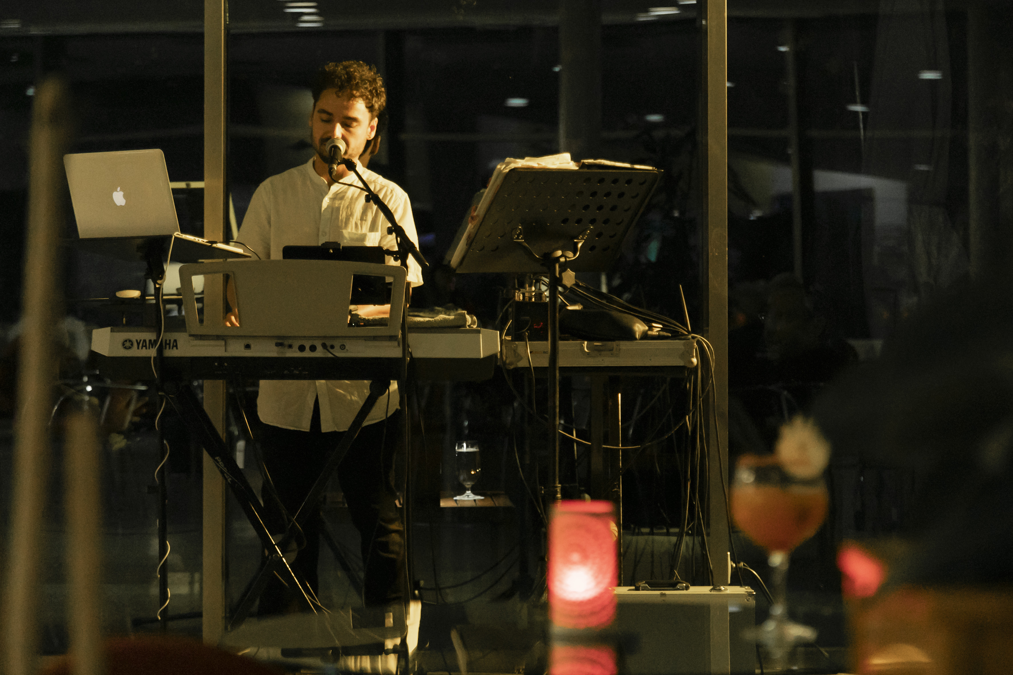 Musician singing into mic while playing Yamaha keyboard with MacBook.