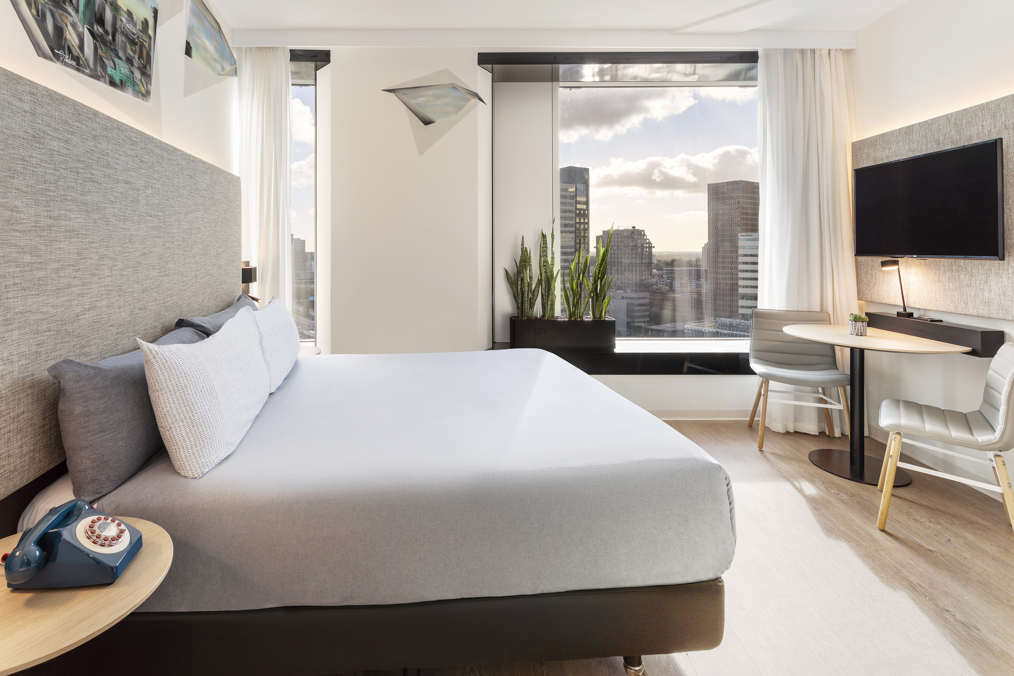 Modern hotel room with city skyline view, king bed, and stylish interior.