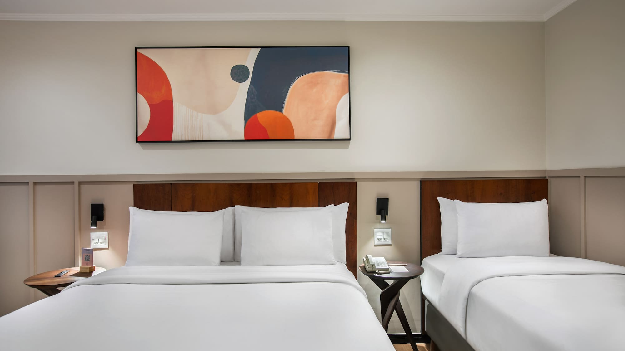 Modern hotel room with two beds, white linens, wooden headboards, abstract art.