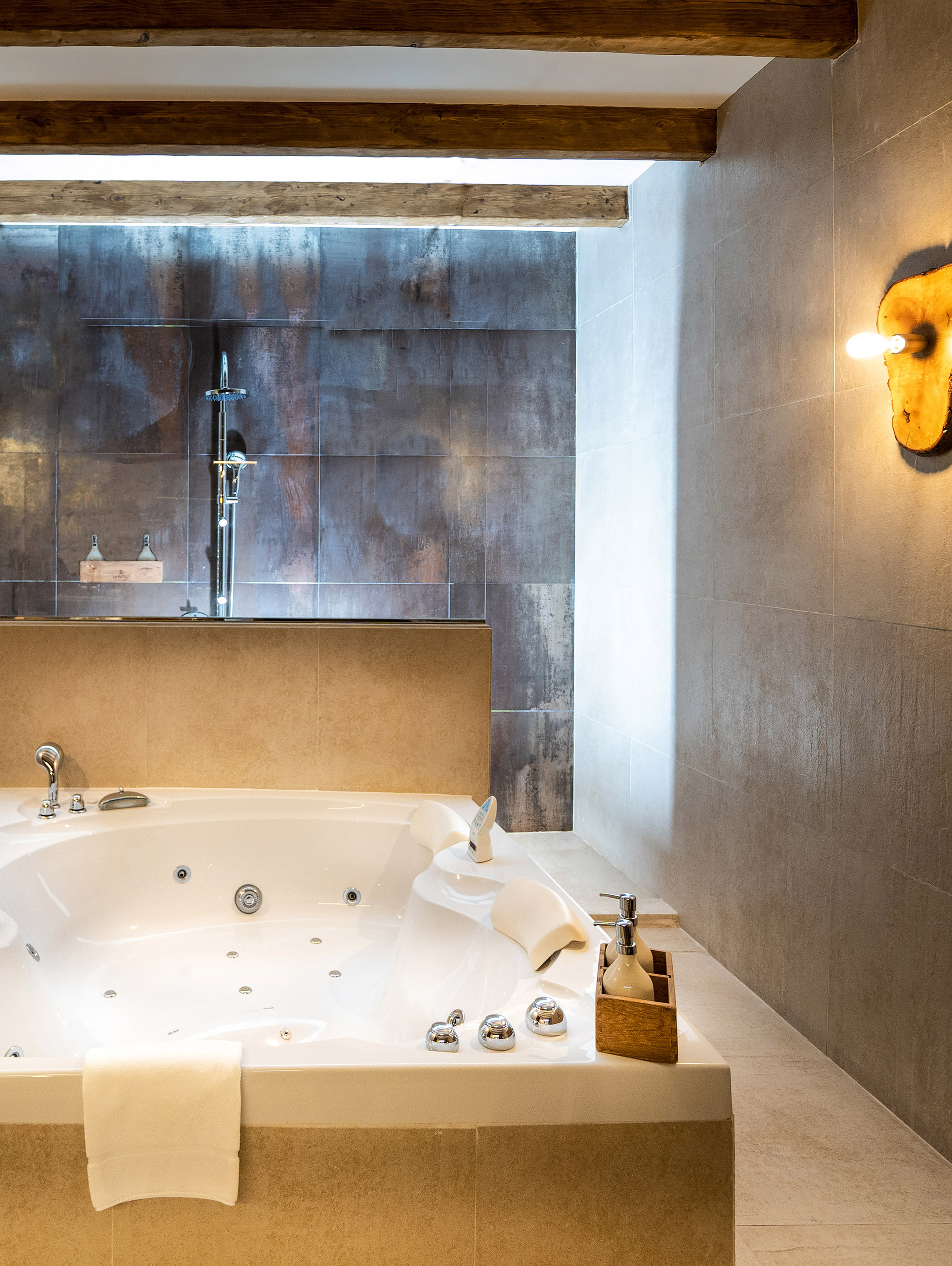 Modern bathroom with white jacuzzi, dark tiled shower, and rustic wooden beams.