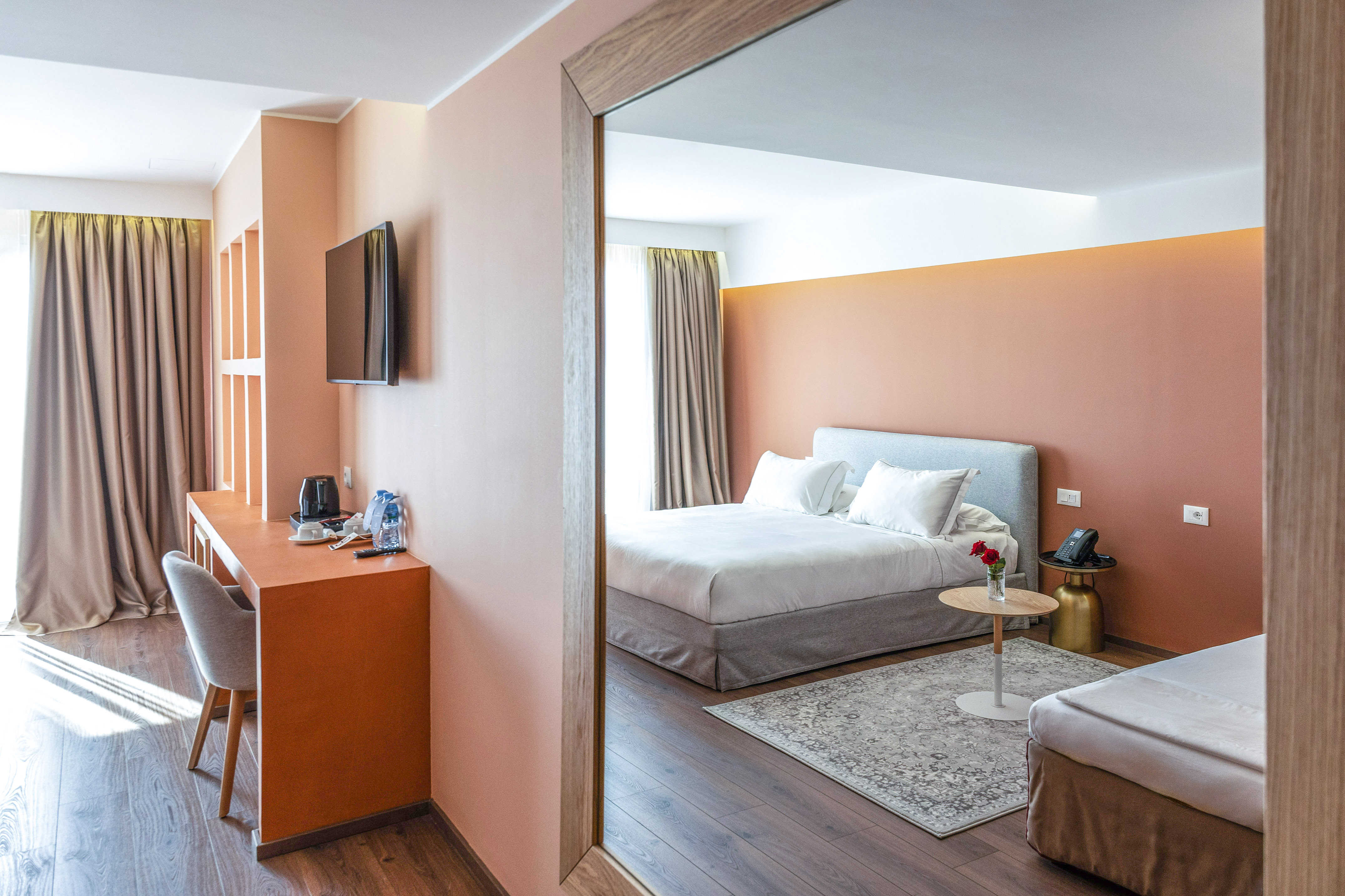 Modern hotel bedroom suite with peach accent walls, bed, and work desk.