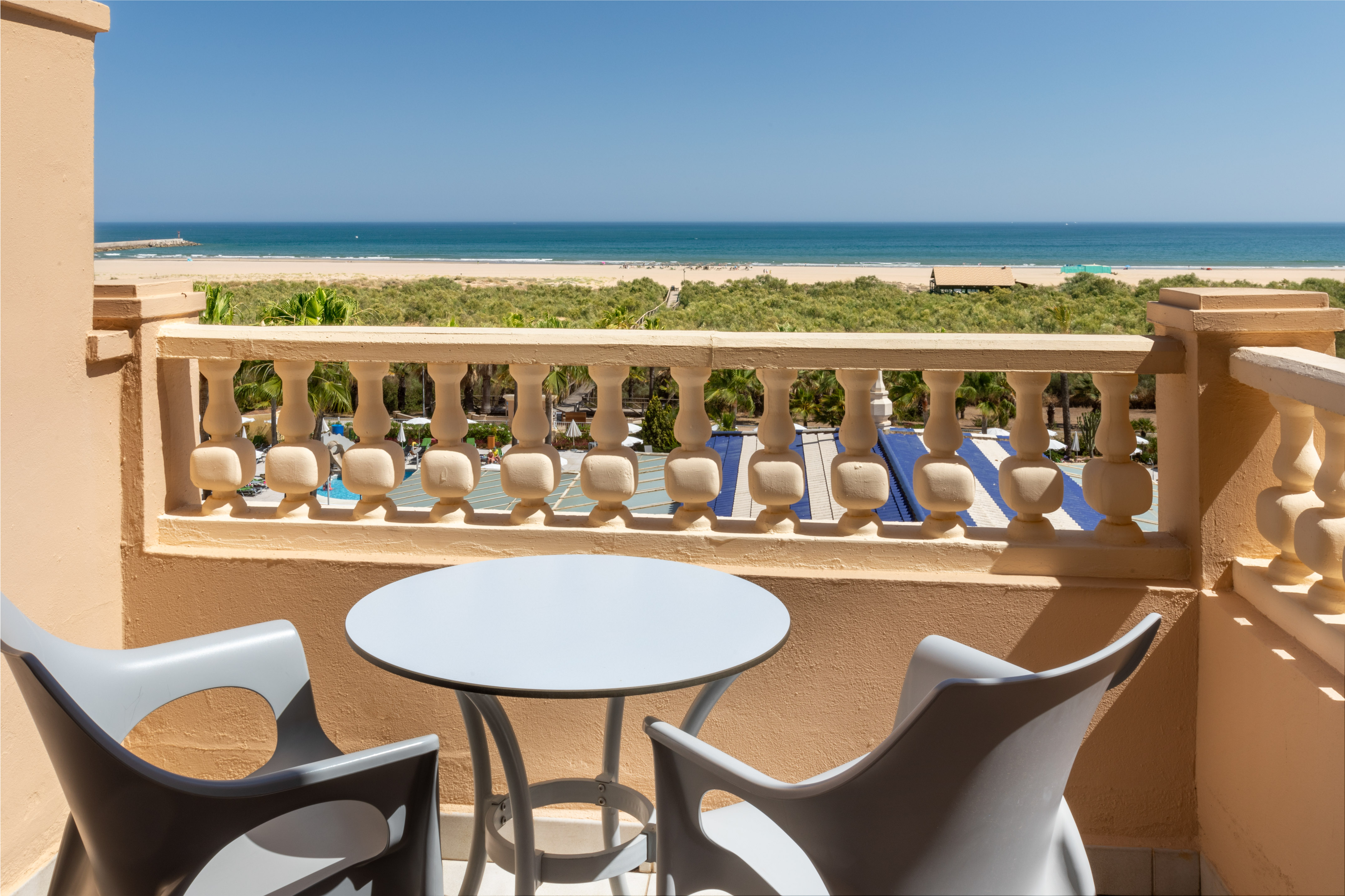 Beachfront hotel balcony with ocean, sandy beach, and green dunes.