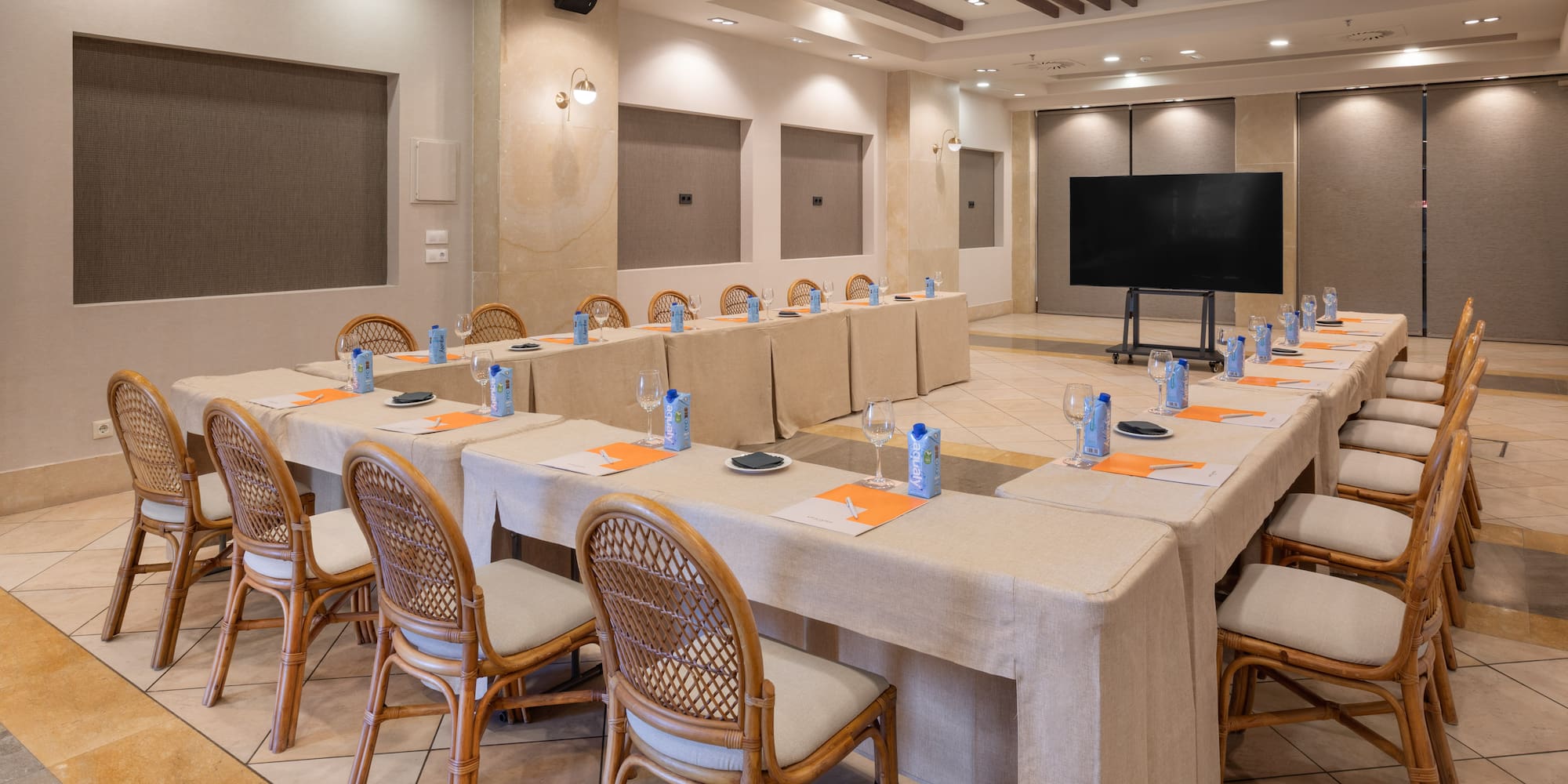 Hotel meeting room: U-shaped tables, rattan chairs, and presentation screen.