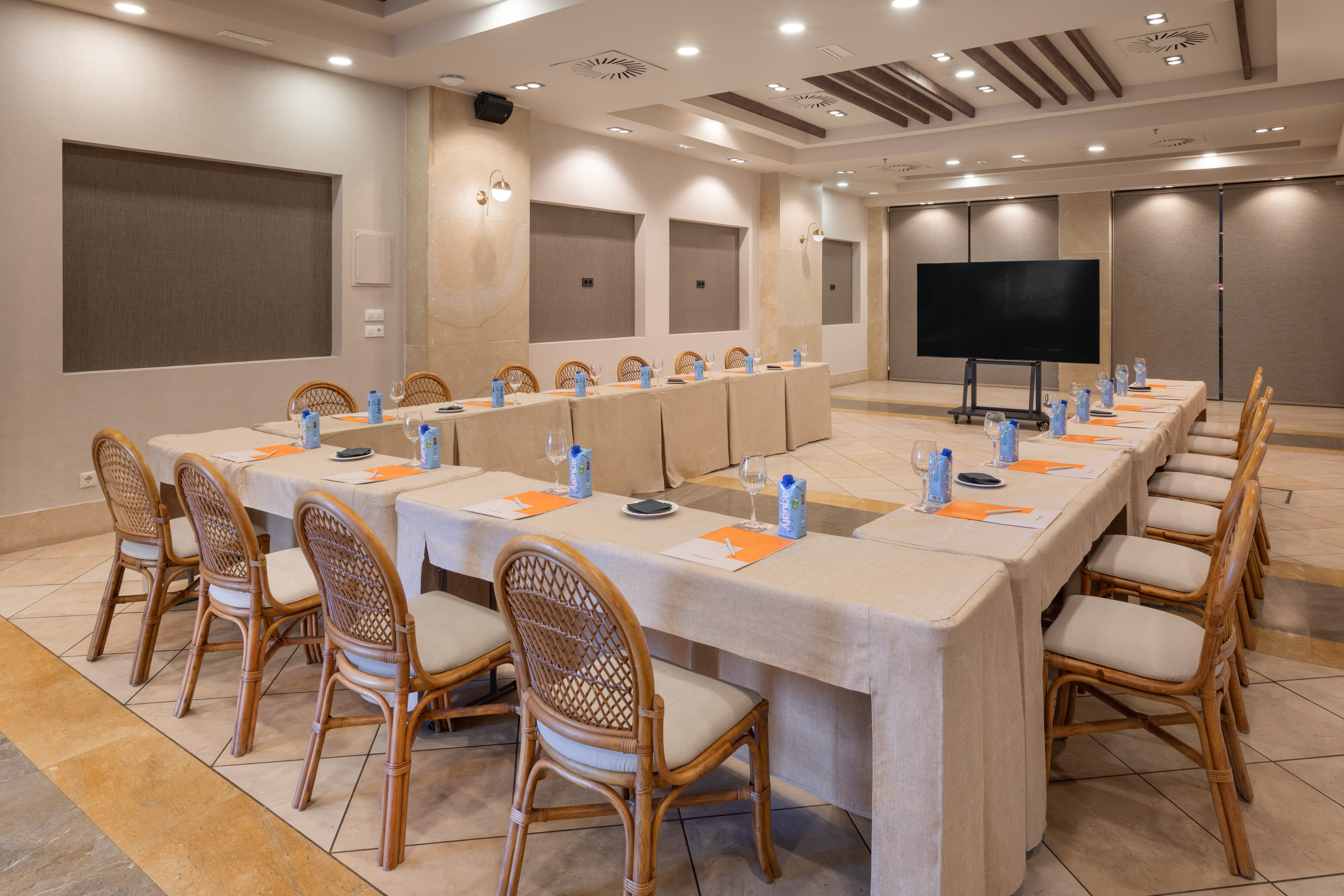Hotel meeting room: U-shaped tables, rattan chairs, and presentation screen.