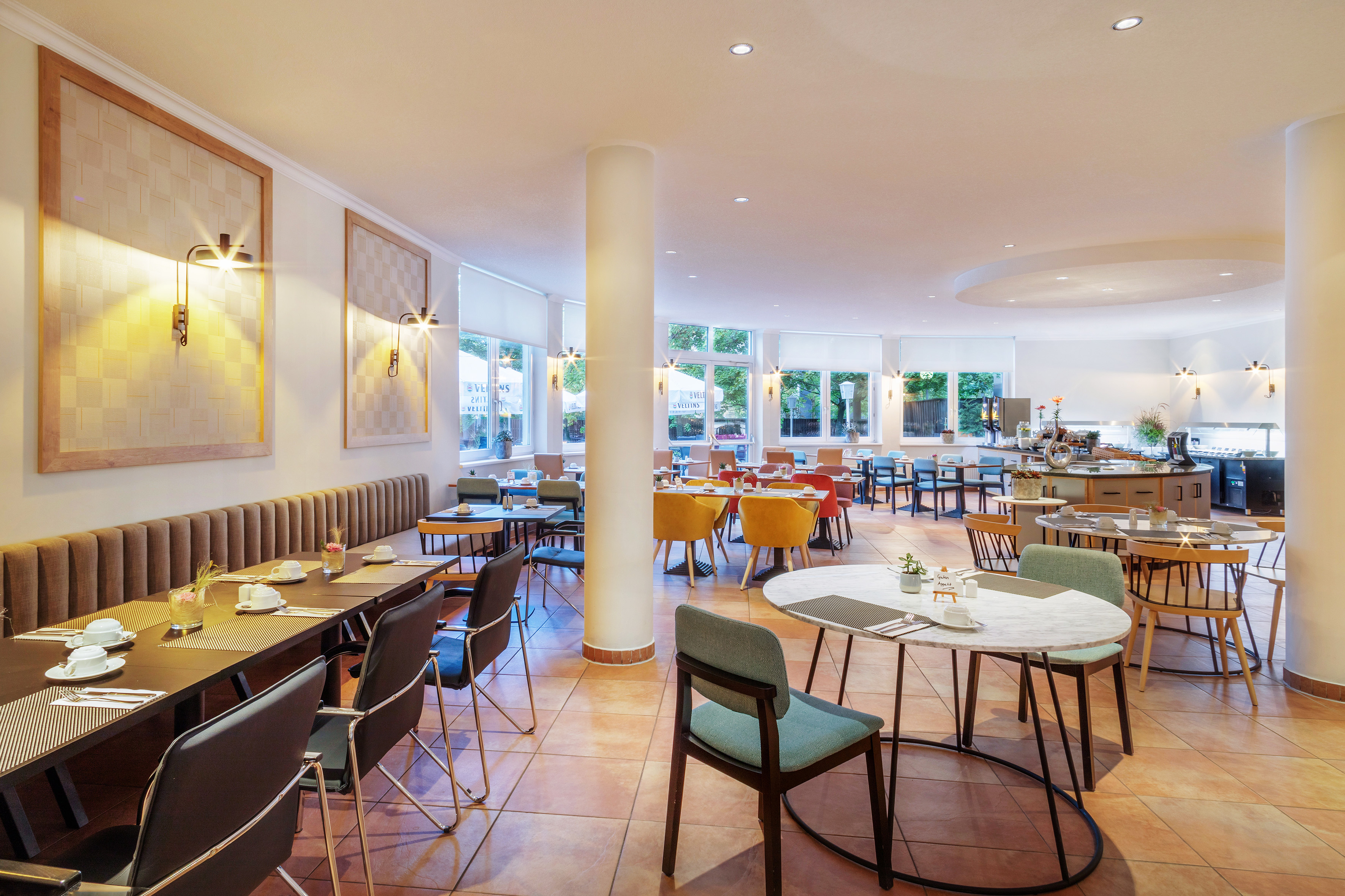 Bright modern hotel restaurant with diverse dining tables and a buffet.
