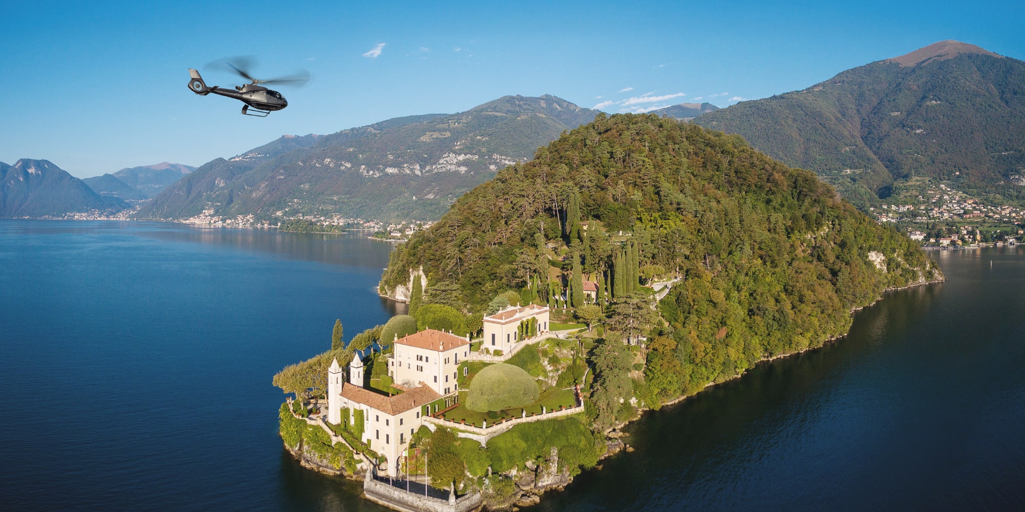 Helicopter flying over luxury villa on Lake Como peninsula.