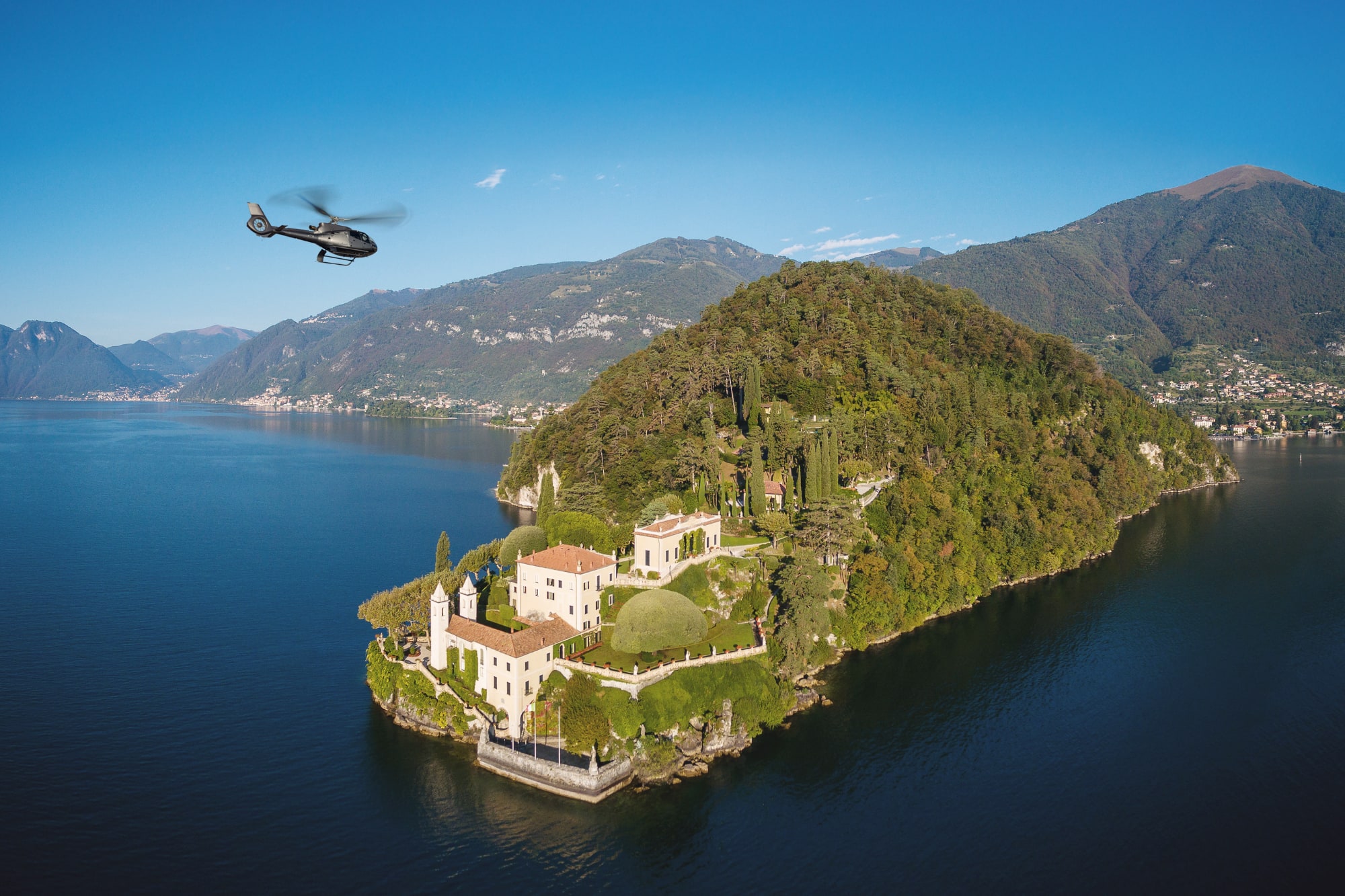 Helicopter flying over luxury villa on Lake Como peninsula.