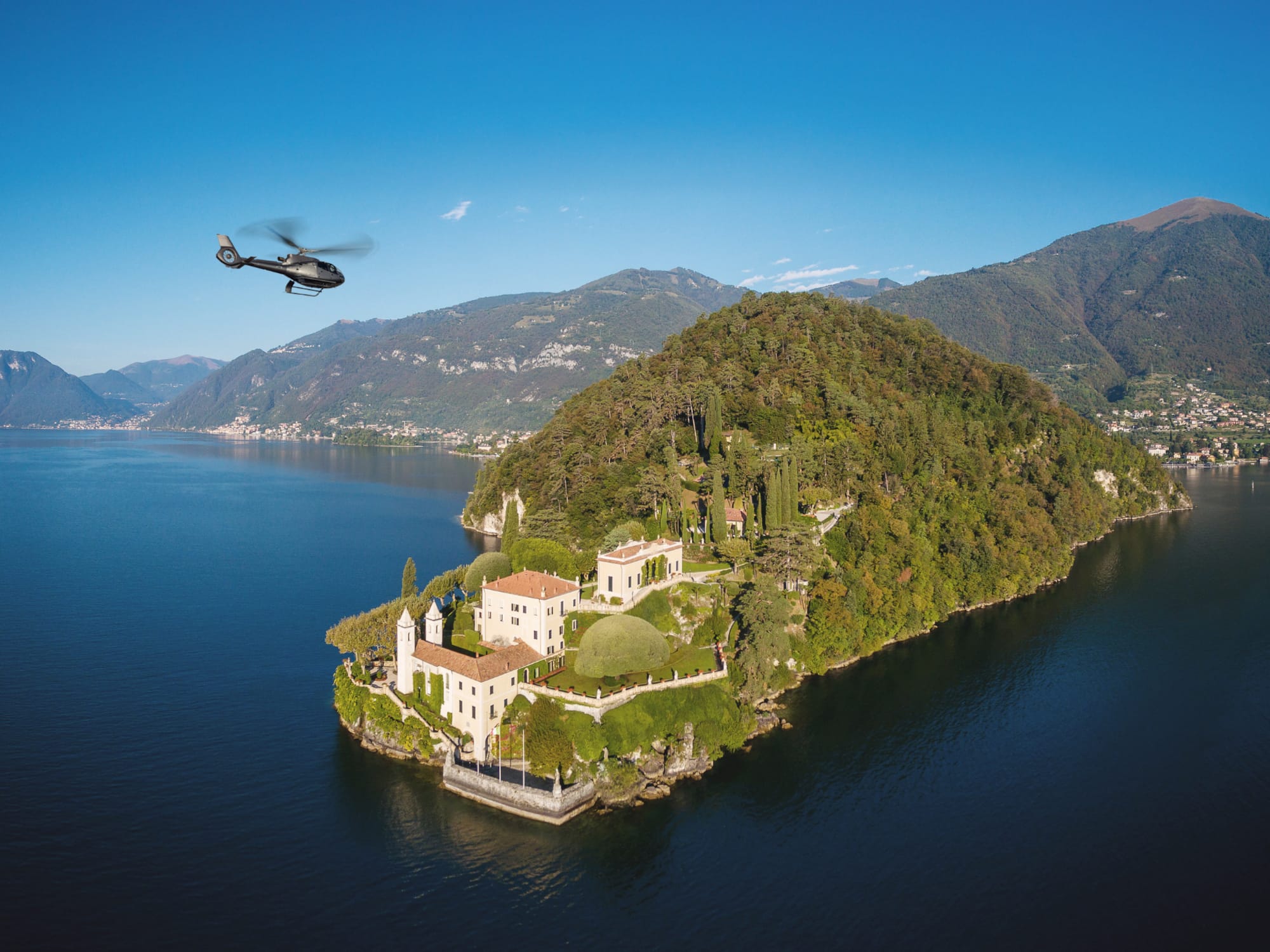 Helicopter flying over luxury villa on Lake Como peninsula.