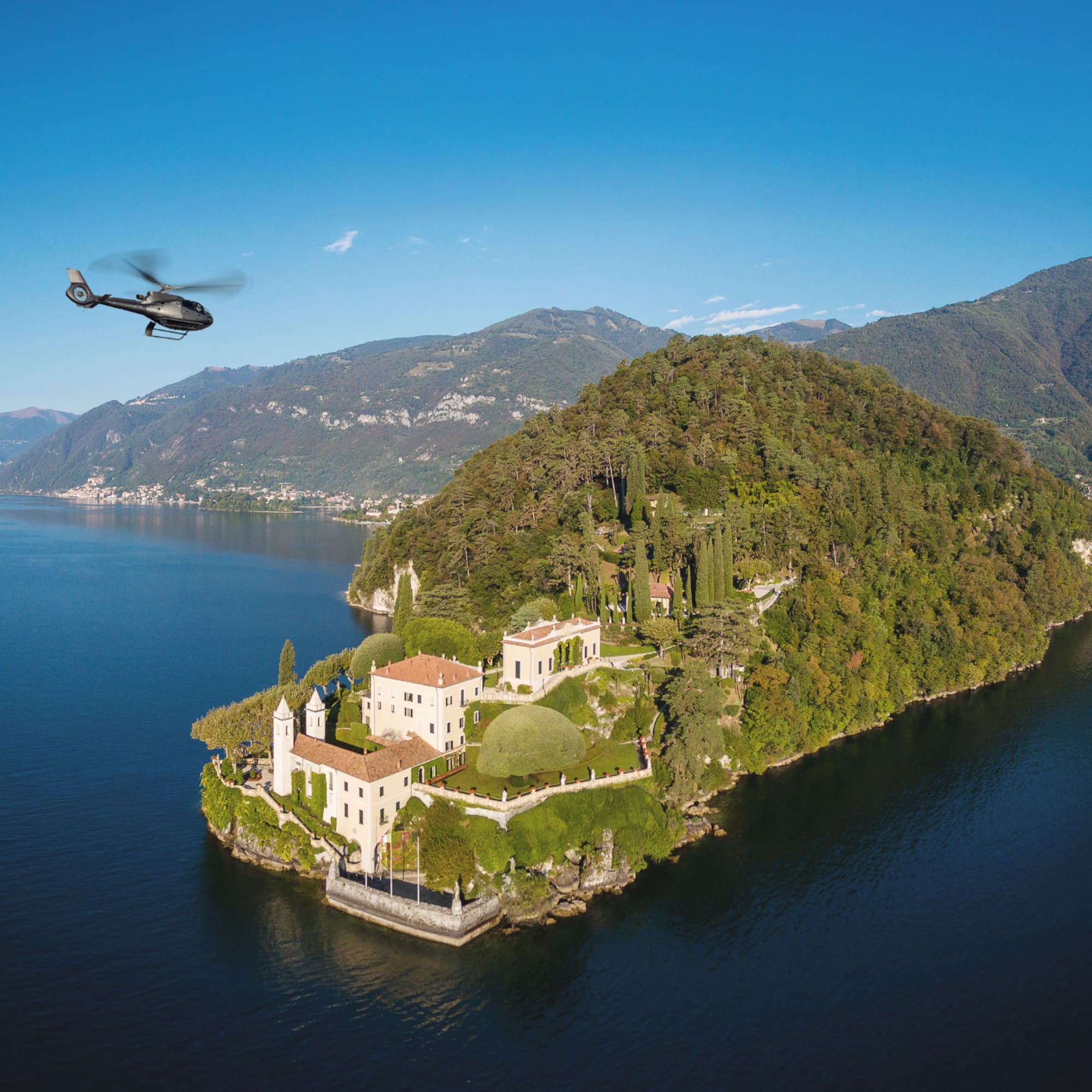 Helicopter flying over luxury villa on Lake Como peninsula.
