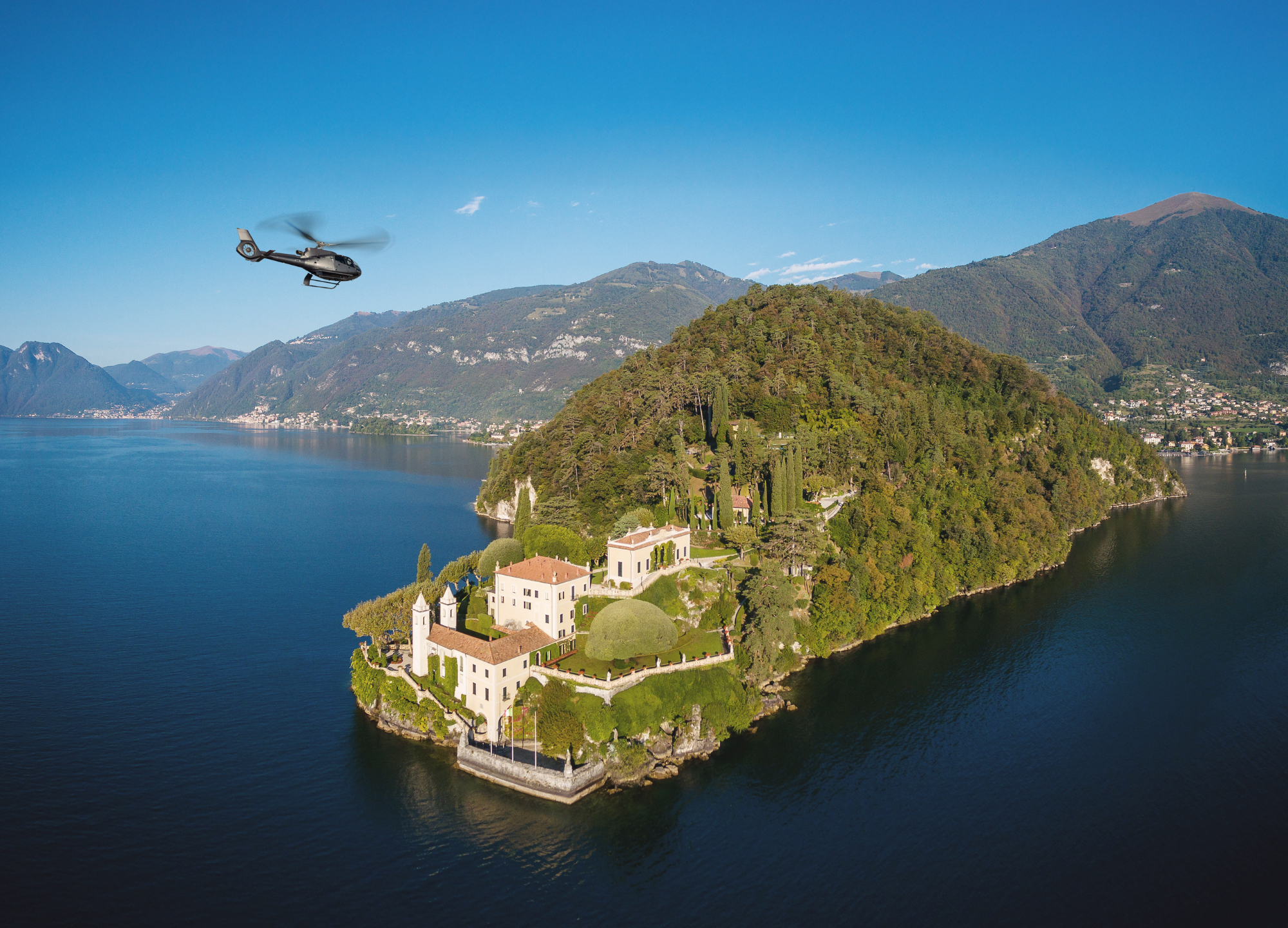 Helicopter flying over luxury villa on Lake Como peninsula.