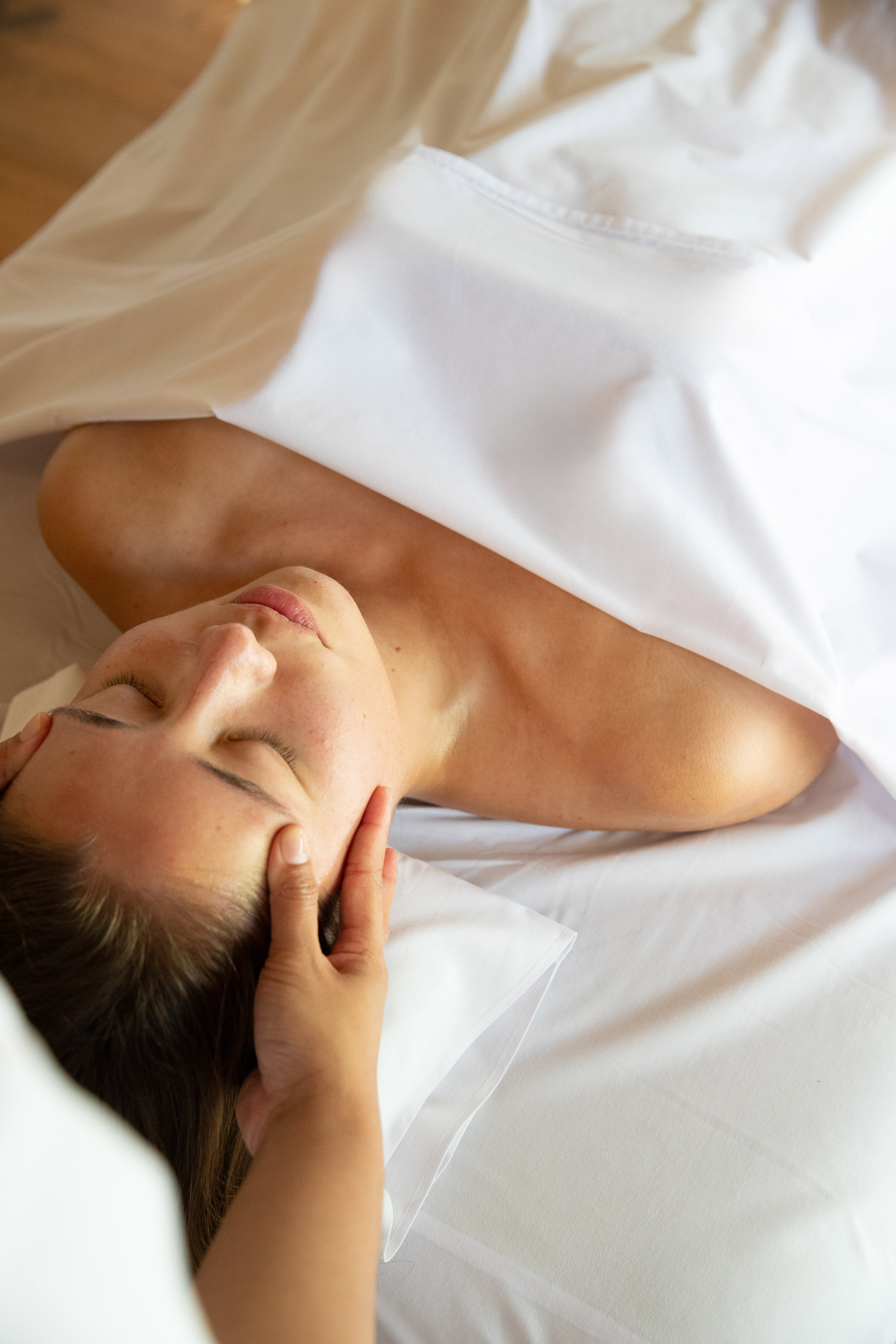 Relaxed woman receiving head massage on white spa bed.