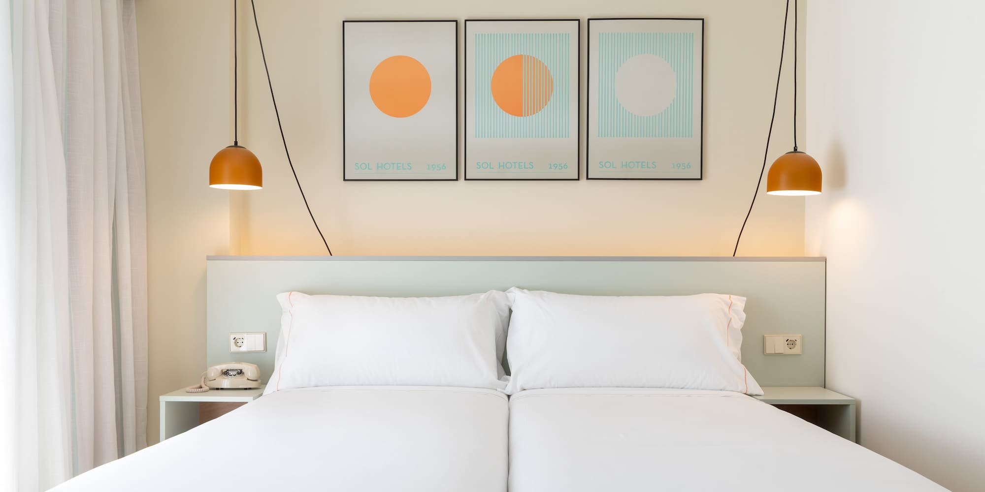 a bed with white sheets and orange lamps above it