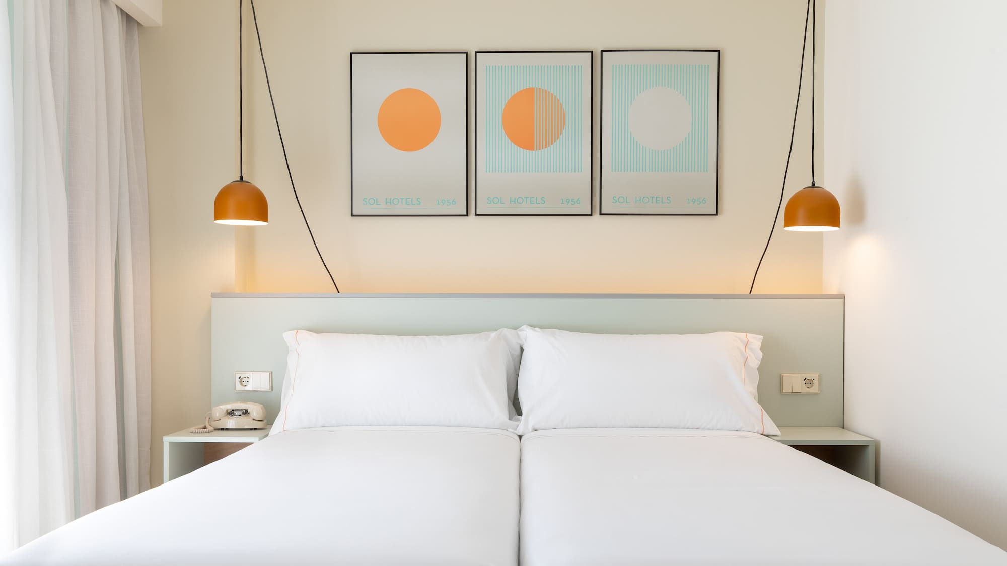 a bed with white sheets and orange lamps above it