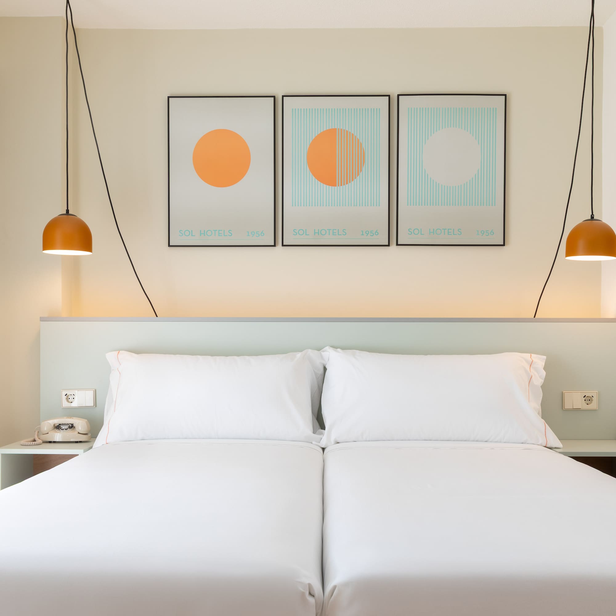 a bed with white sheets and orange lamps above it