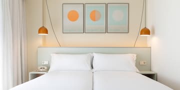 a bed with white sheets and orange lamps above it
