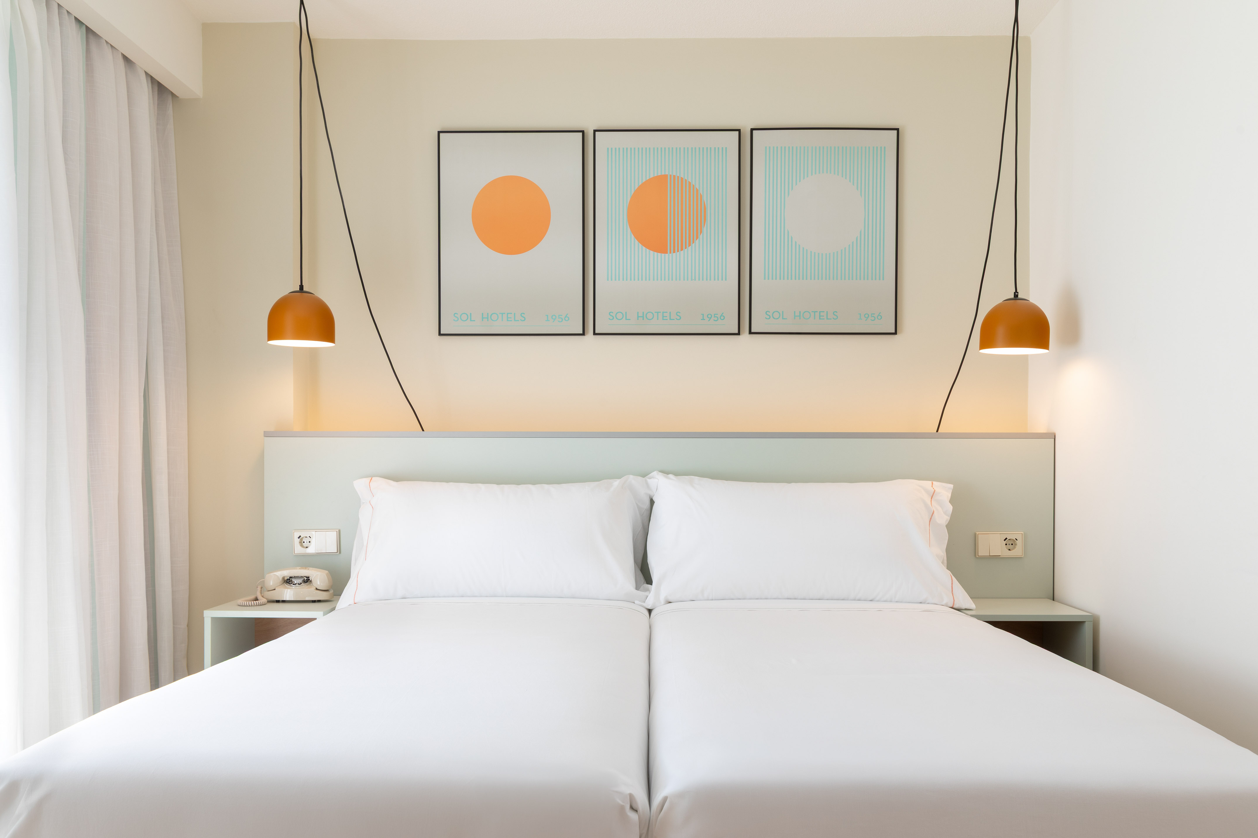 Modern hotel room with twin beds, minimalist decor, abstract art, pendant lights.